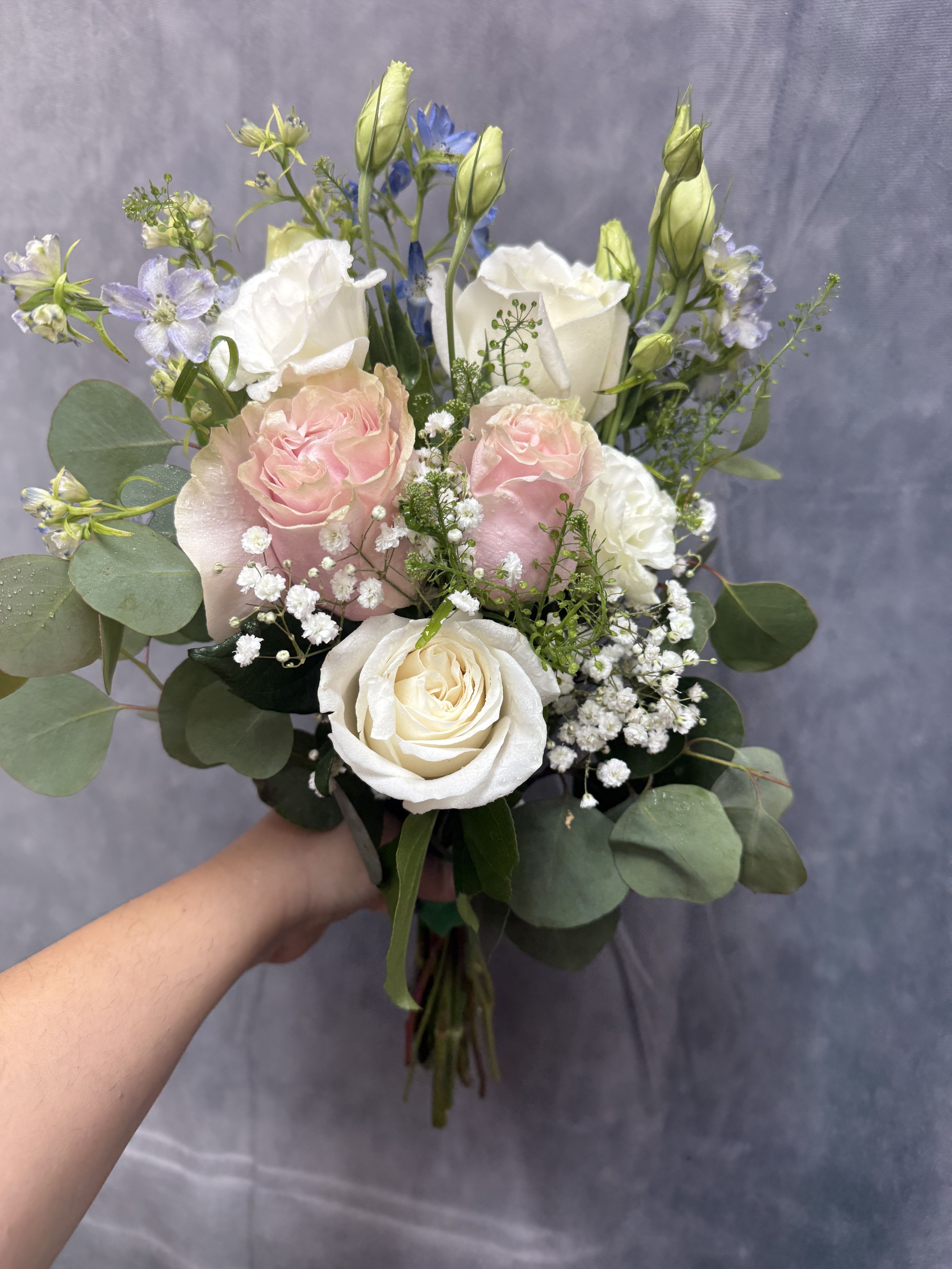 Whispering blush prom bouquet  - Soft white and blush roses with pale blue delphinium, lisianthus and baby's breath, layered with eucalyptus beautifully wrapped for prom