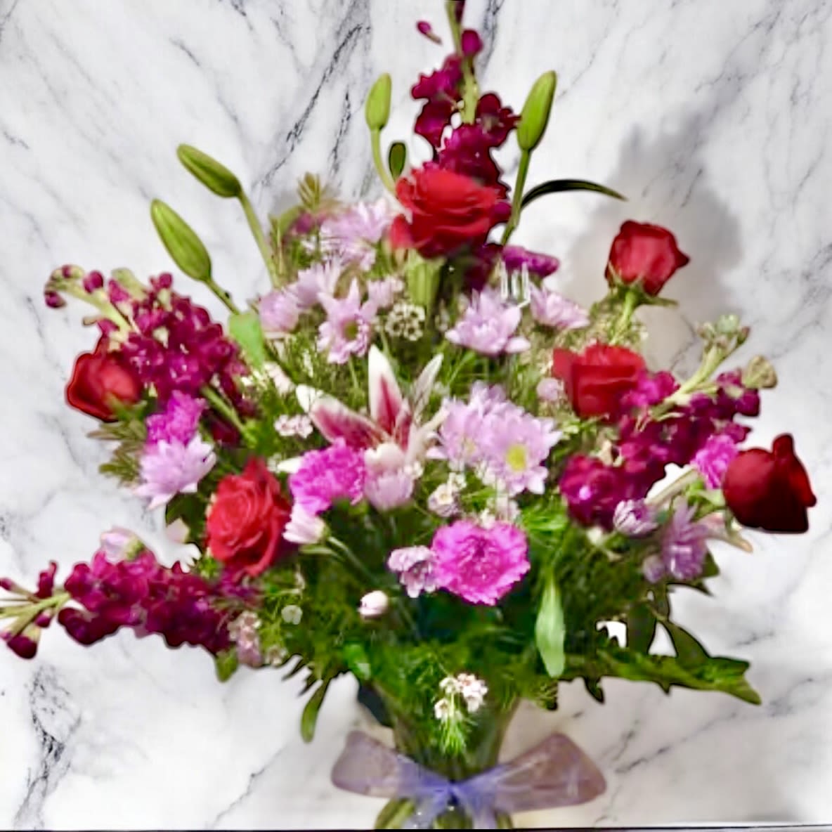 Mixed bouquet of pink and red flowers with a purple ribbon