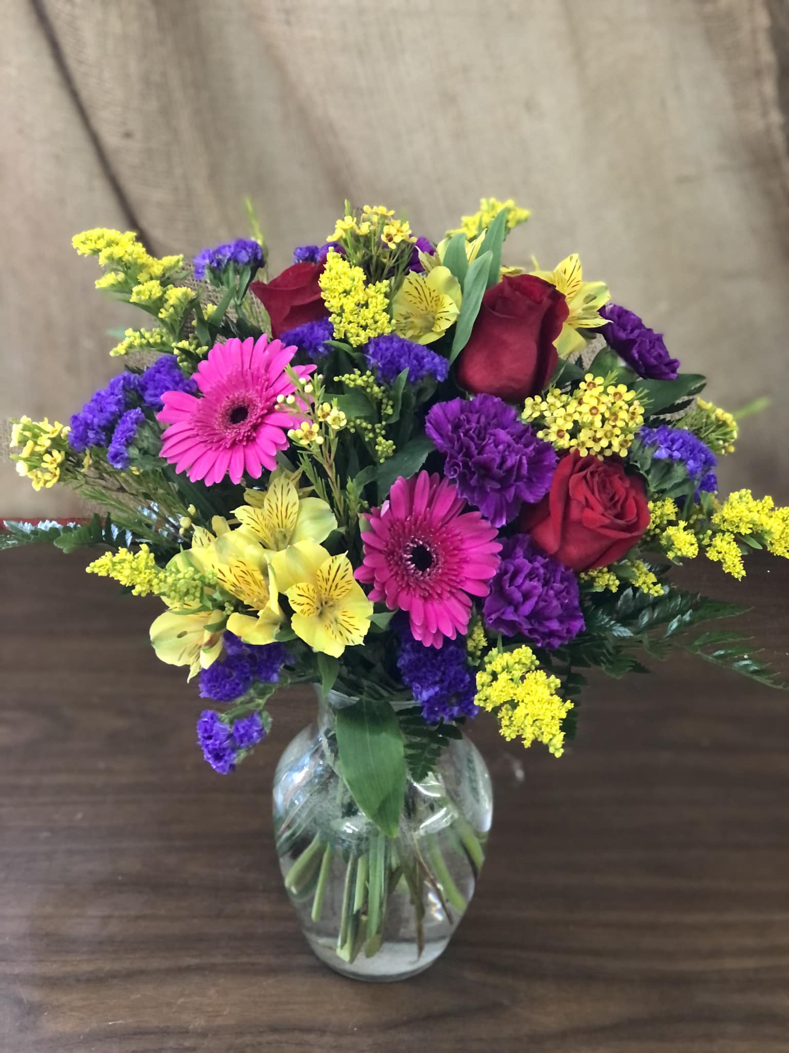 Mixed bouquet of red roses, pink gerbera daisies, and yellow and purple flowers in a glass vase