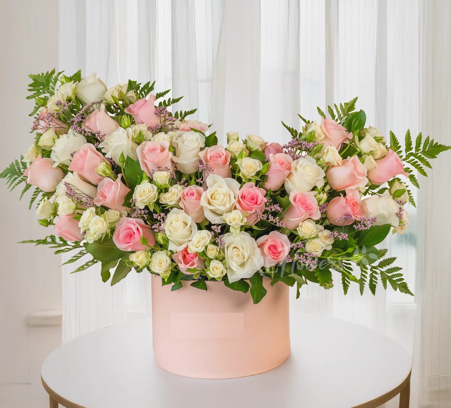 Pink and white roses arranged in a blush round box