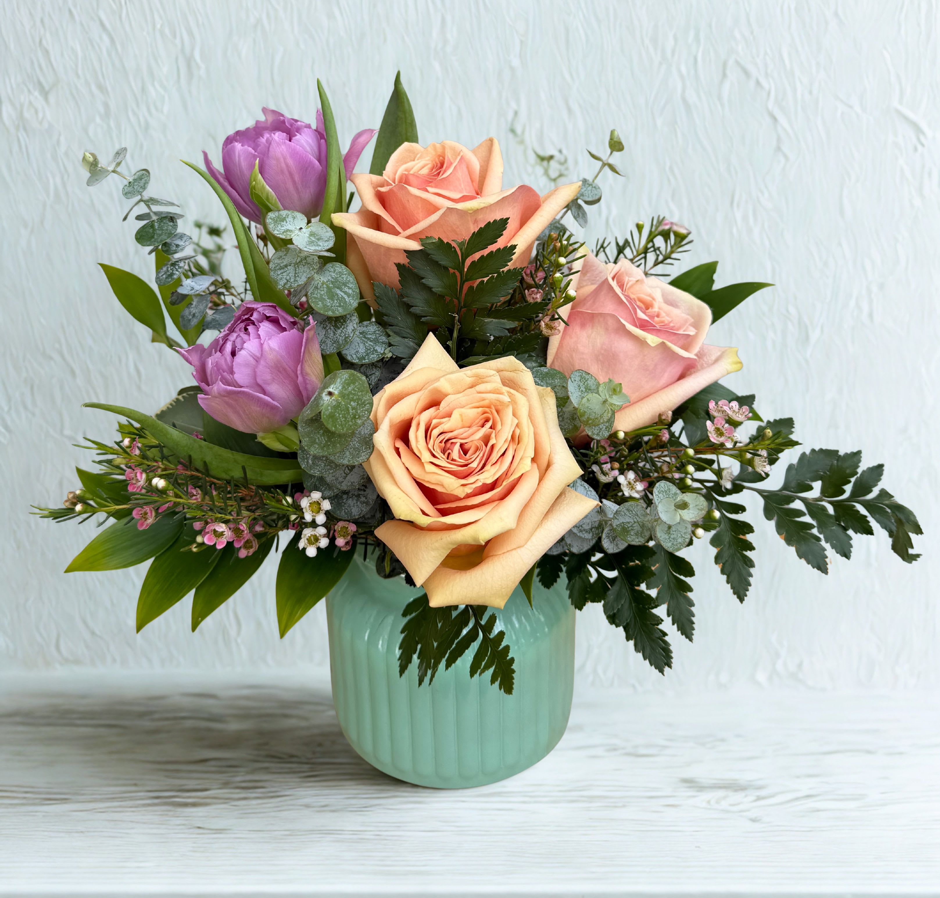 Peachy Keen  - A charming blend of soft, romantic hues, this arrangement features lush peach roses paired with delicate lavender tulips, accented by airy greenery and petite filler blooms. Vase Color may vary