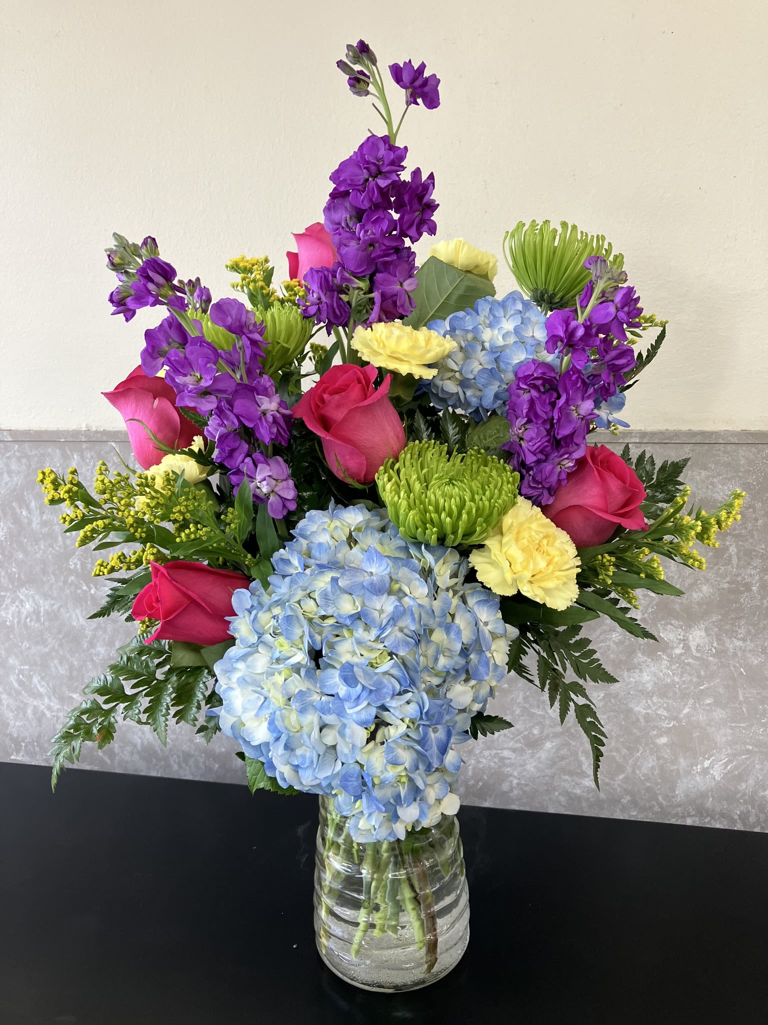 Colorful bouquet of roses, hydrangeas, and purple blooms in a glass vase