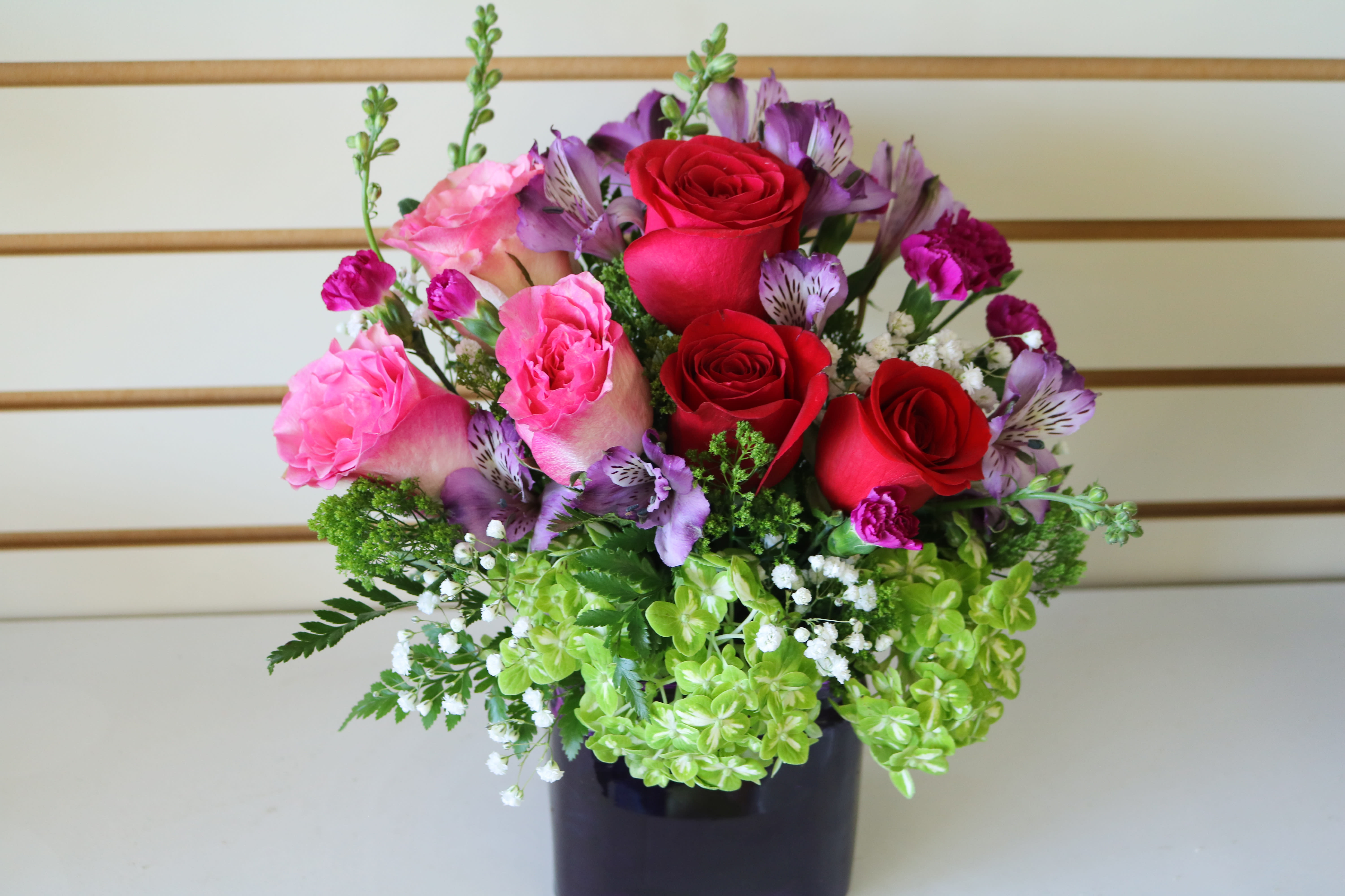 Bouquet of red and pink roses with purple flowers in a dark vase