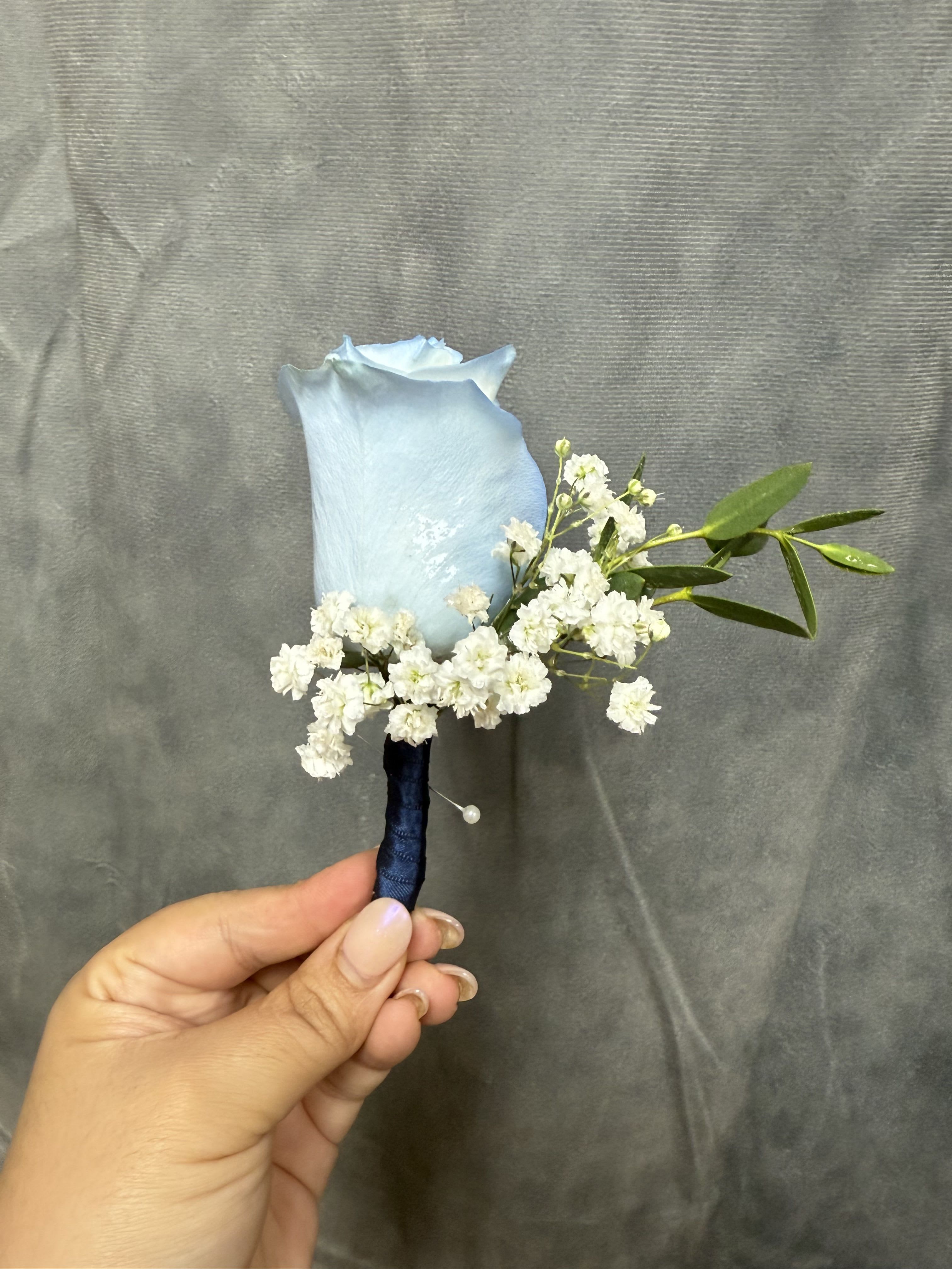 Baby blue boutonnière  - Baby blue rose boutonniere with white filler and green leaves, stem wrapped in dark blue ribbon