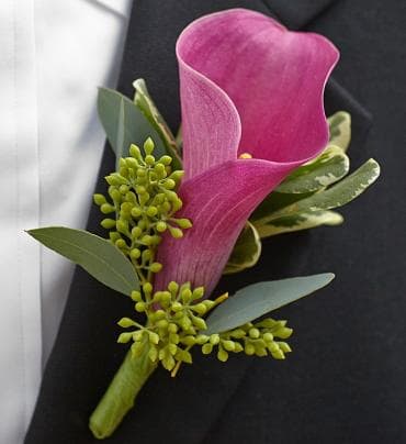 Pink calla lily boutonniere with green accents on a dark suit