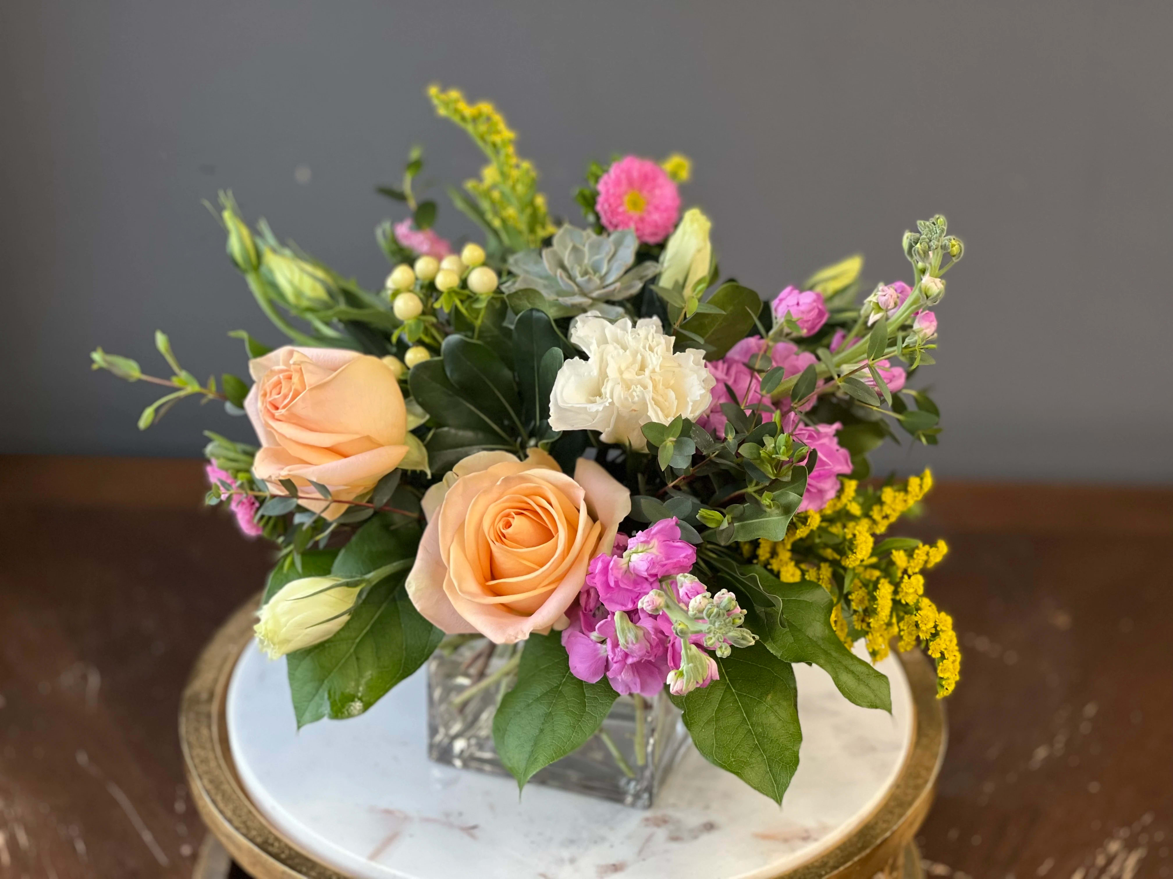 Peach roses and pink flowers in a square glass vase