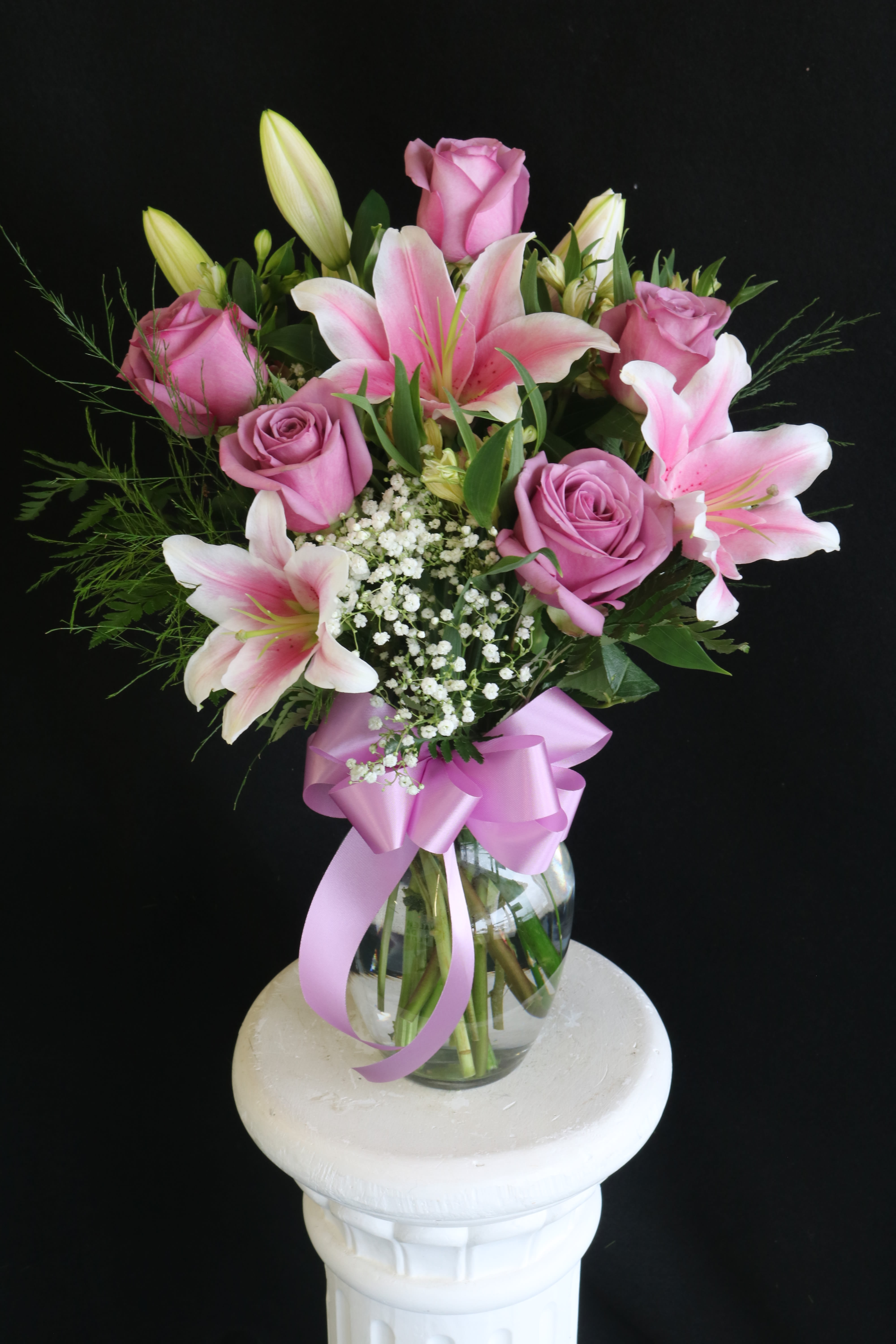 Pink roses and lilies in a glass vase with a pink ribbon