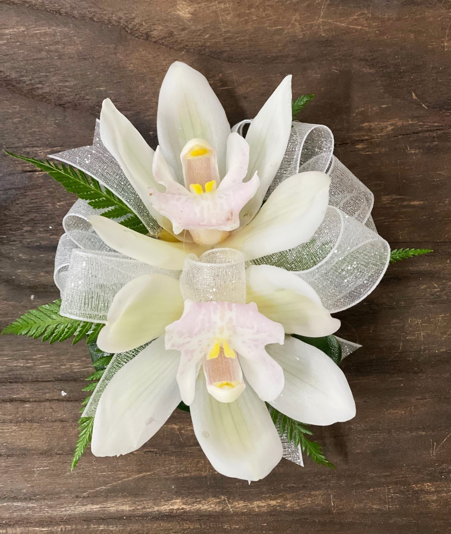 White orchid corsage with silver ribbon on a wooden surface