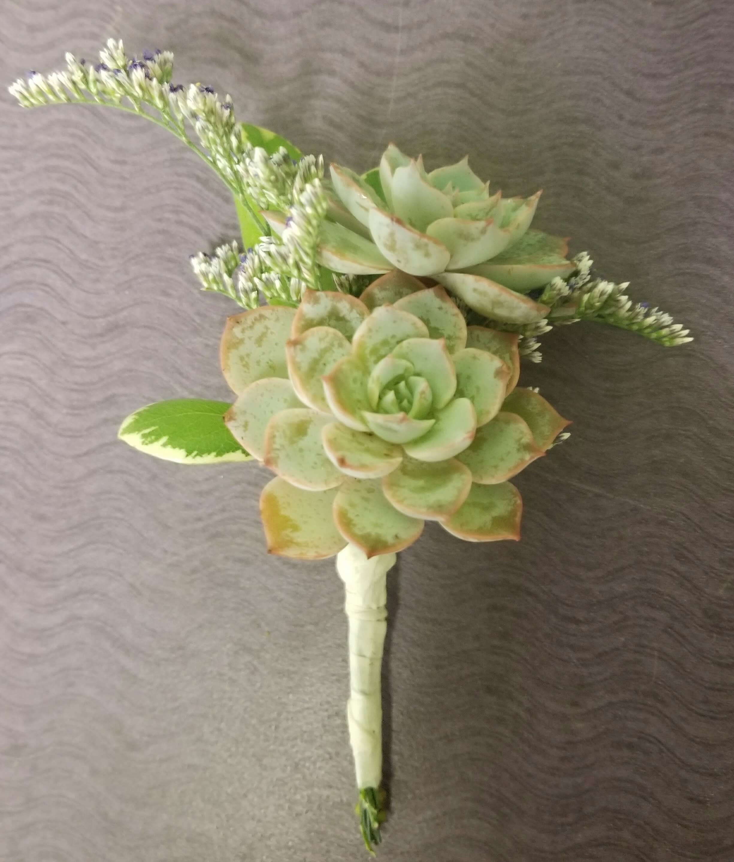 Succulent boutonniere with pale green rosettes and small white filler flowers