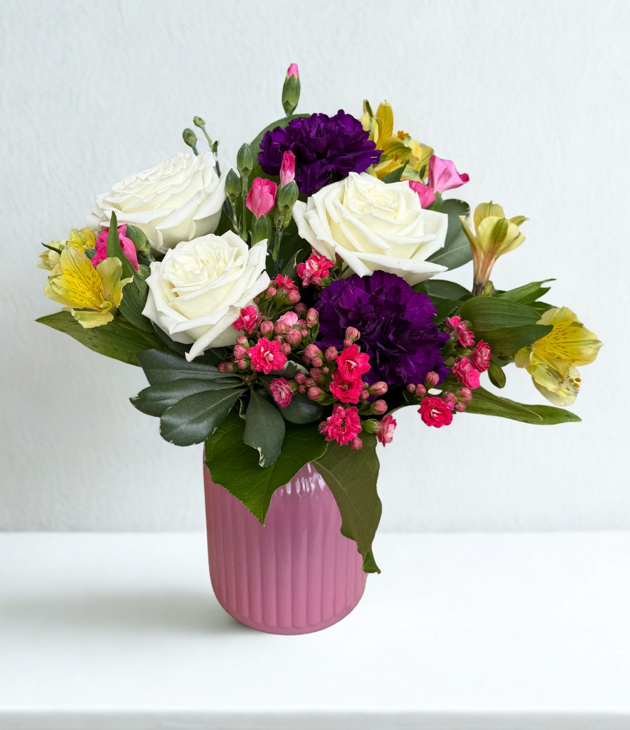 Sweet &amp; Simple  - A Bright and elegant mix of white roses, purple carnations and yellow accents arranged with lush greens in a modern vase. Color of vase may vary.