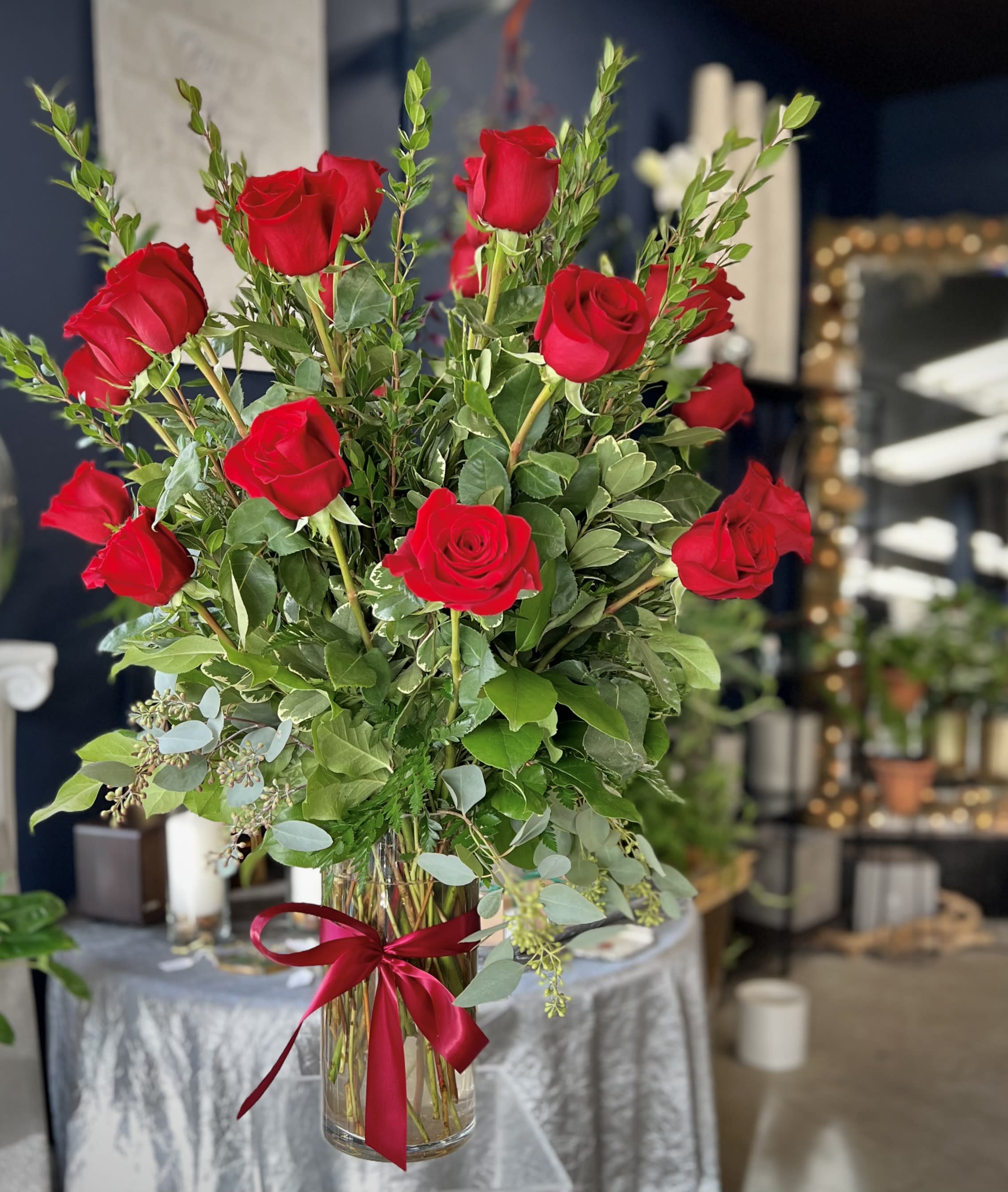 Tall vase arrangement of red roses with mixed greenery and a red ribbon