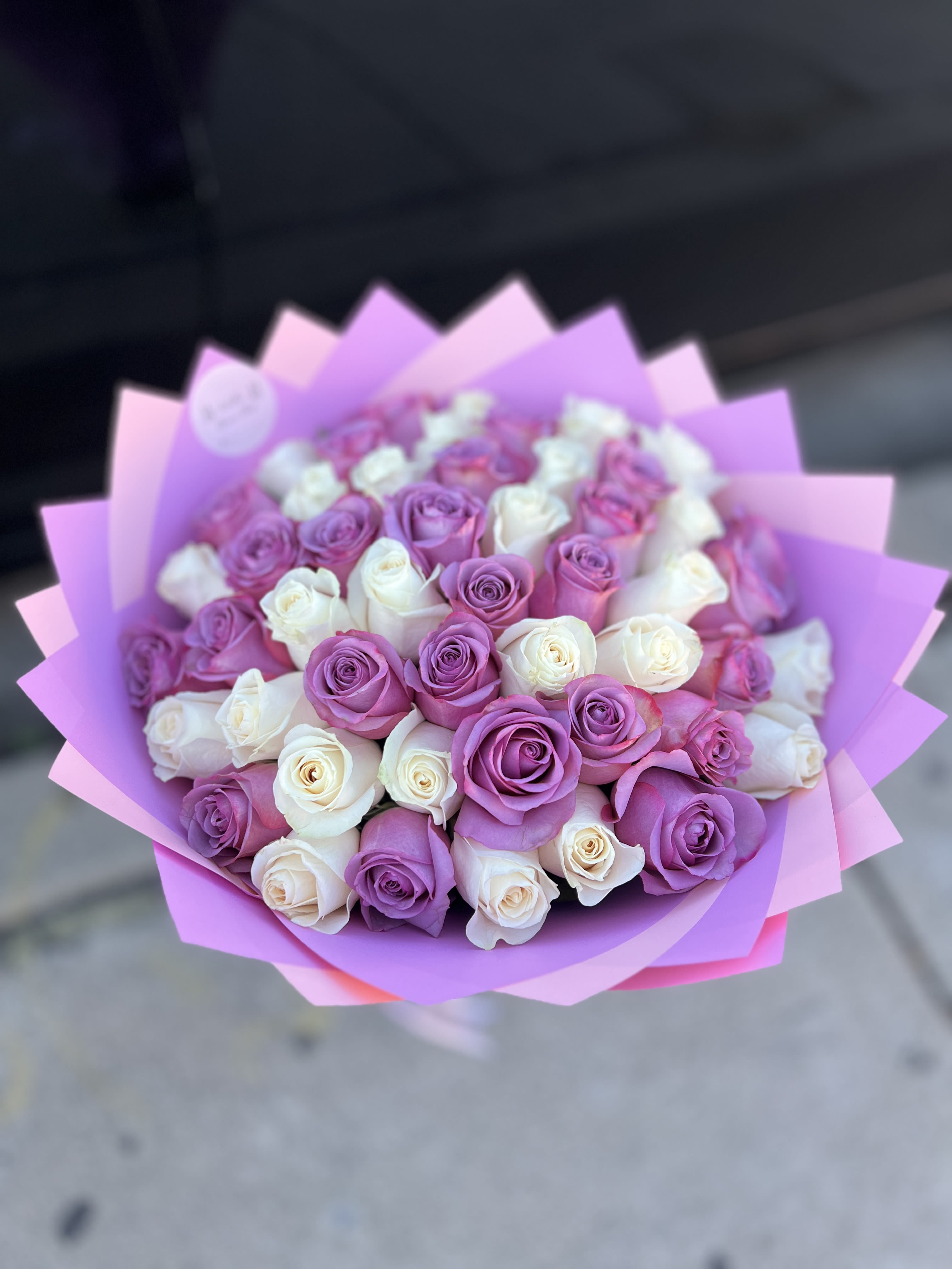Bouquet of pink, purple, and white roses wrapped in pink paper