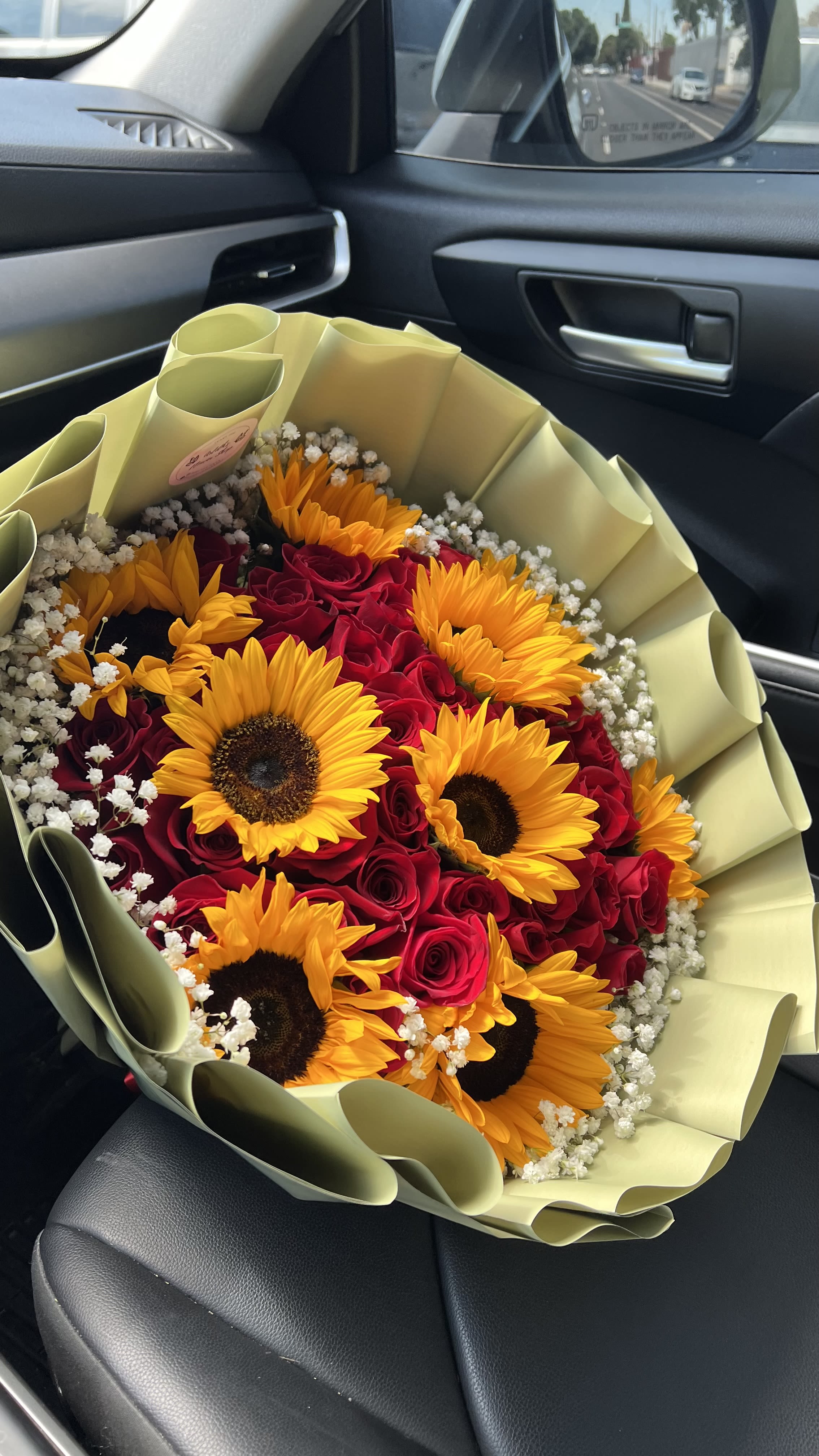 Bouquet of red roses and yellow sunflowers wrapped in pale paper