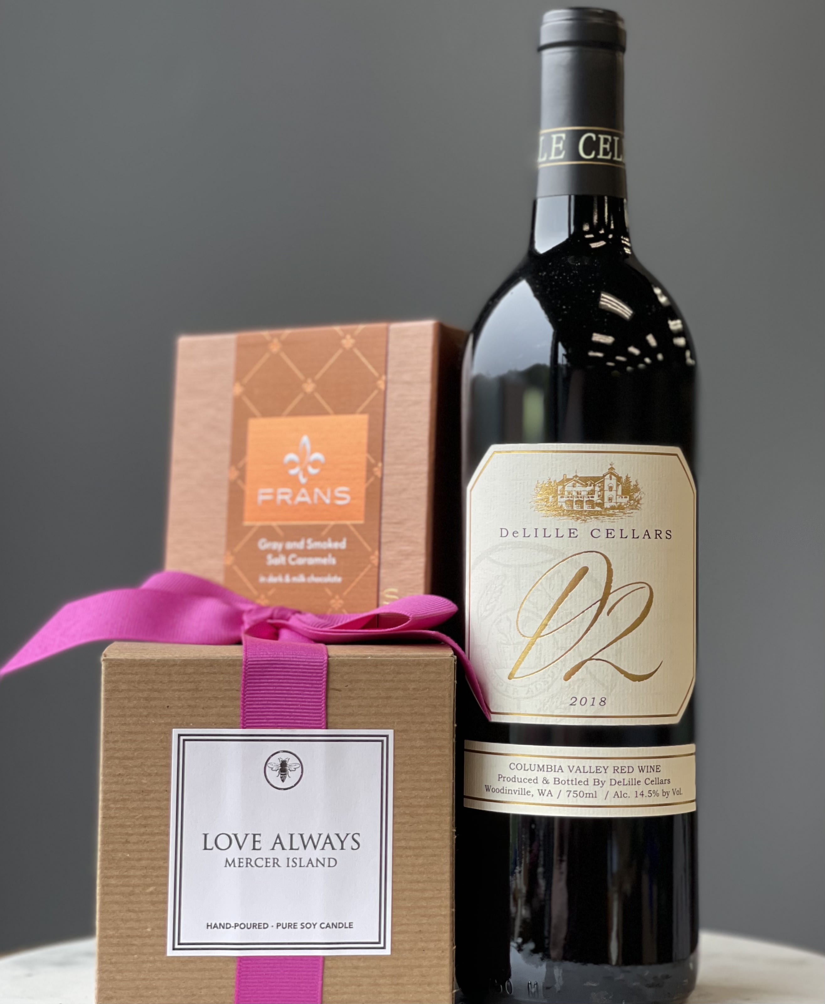 Wine bottle with two boxed gift items tied with a pink ribbon