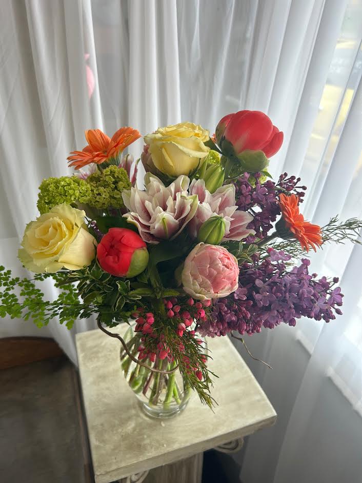 Mixed bouquet of roses, lilies, and purple blooms in a clear glass vase
