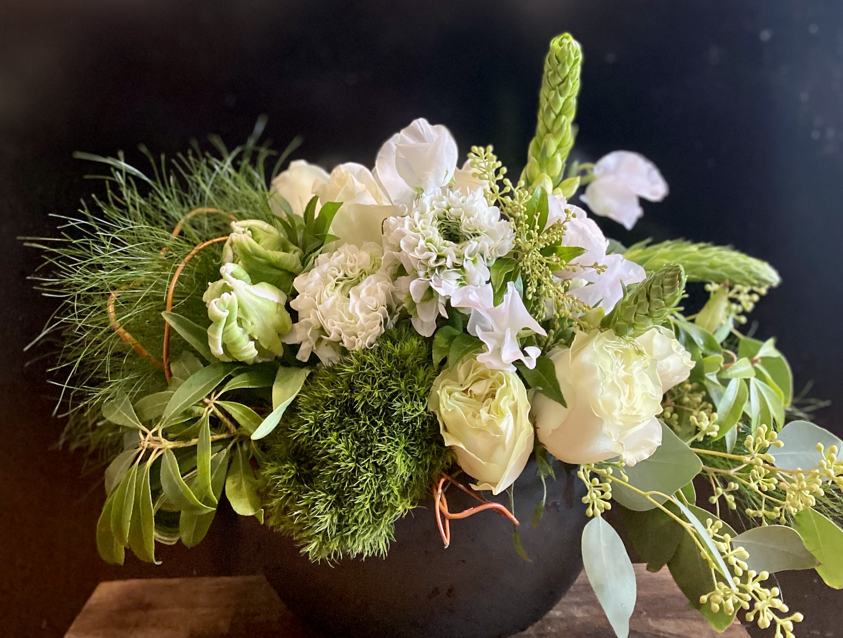 White floral arrangement in a black vase with green accents