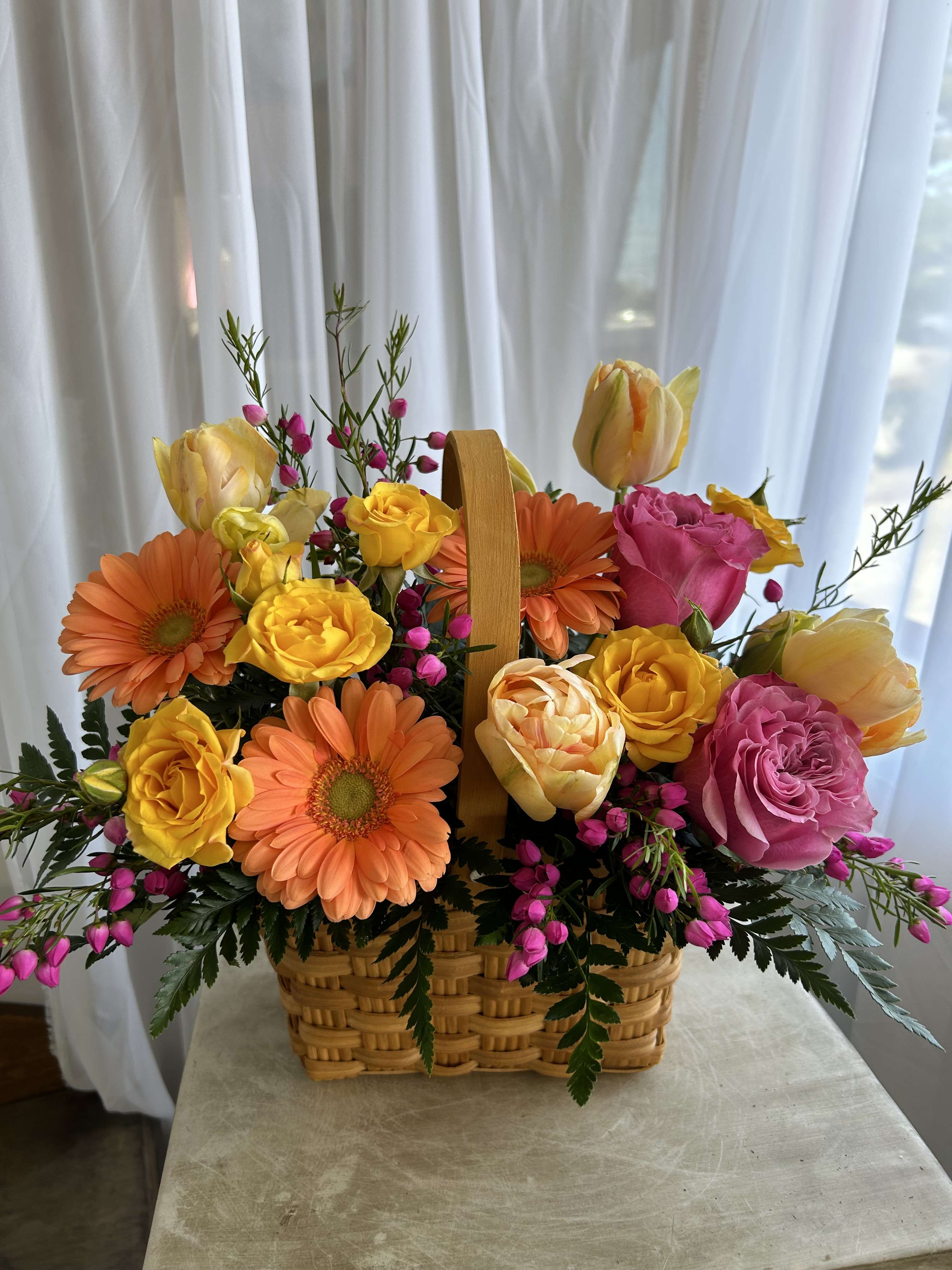 Basket of orange gerberas and yellow, pink, and peach roses