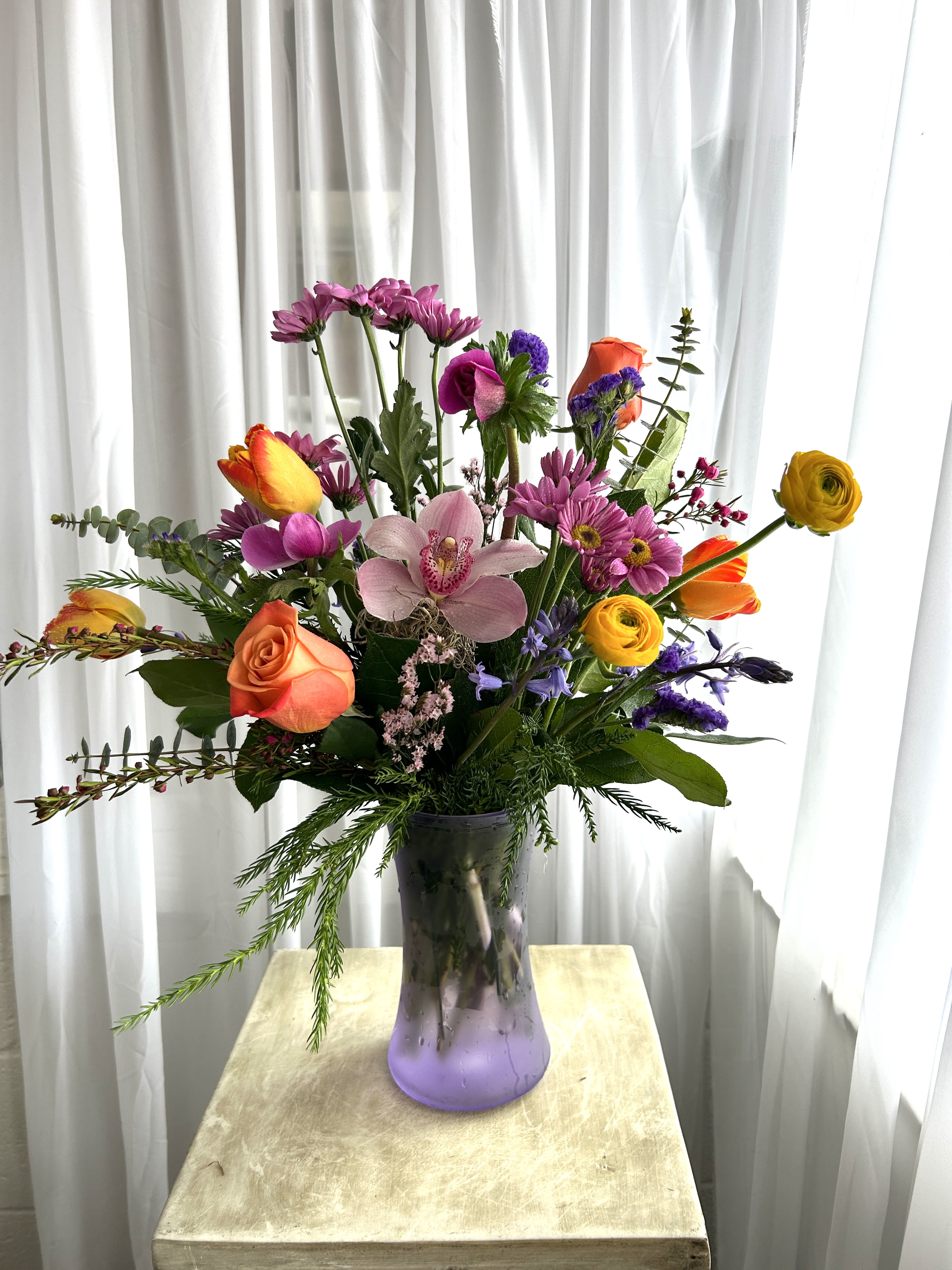 Mixed bouquet in a purple glass vase with roses, orchids, and daisies