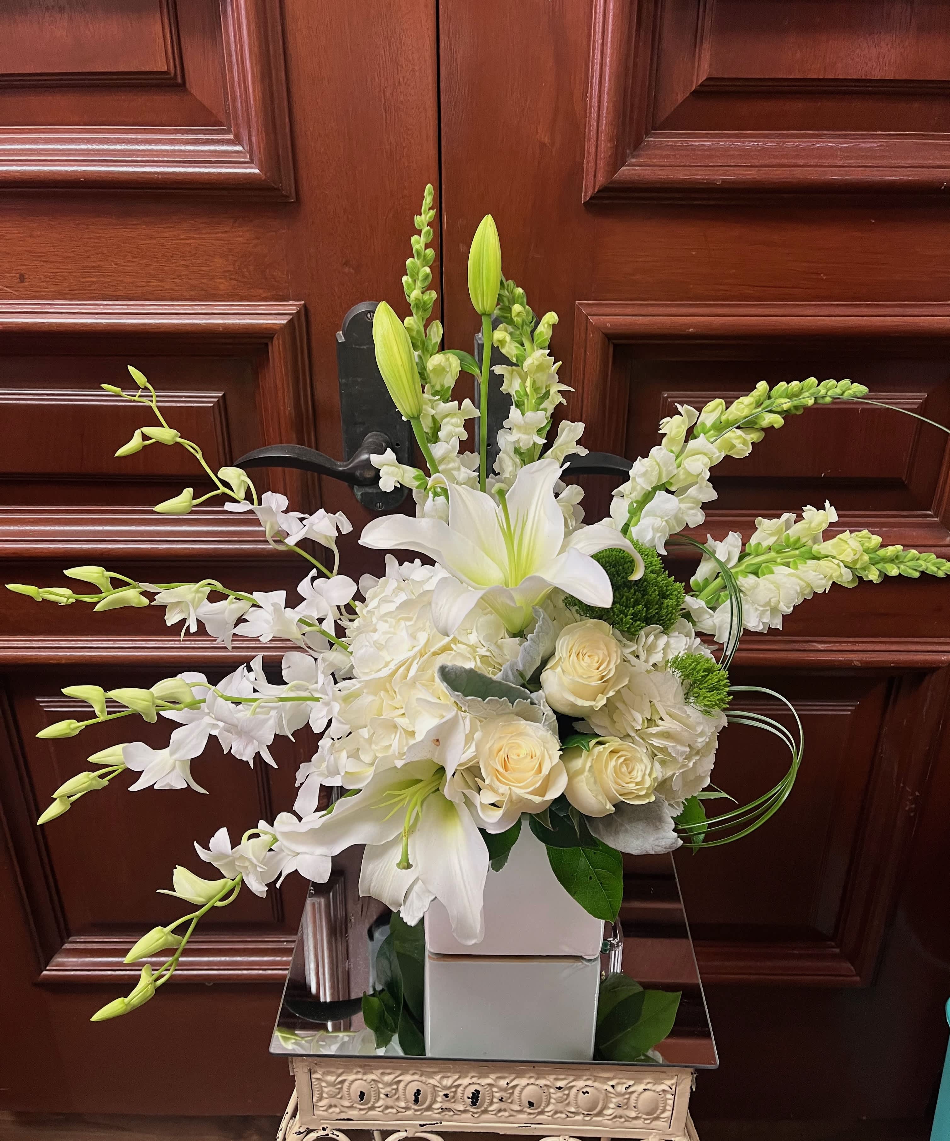 Celebrate Life - Recipe: White Hydrangea, White Roses, White Asiatic Lillies, White Phalaenopsis Orchids, Green Cushion Mums Dusty Miller, and succulent in white vase. Availability: All year round Design View: Front Facing View Photo available: Standard and Premium