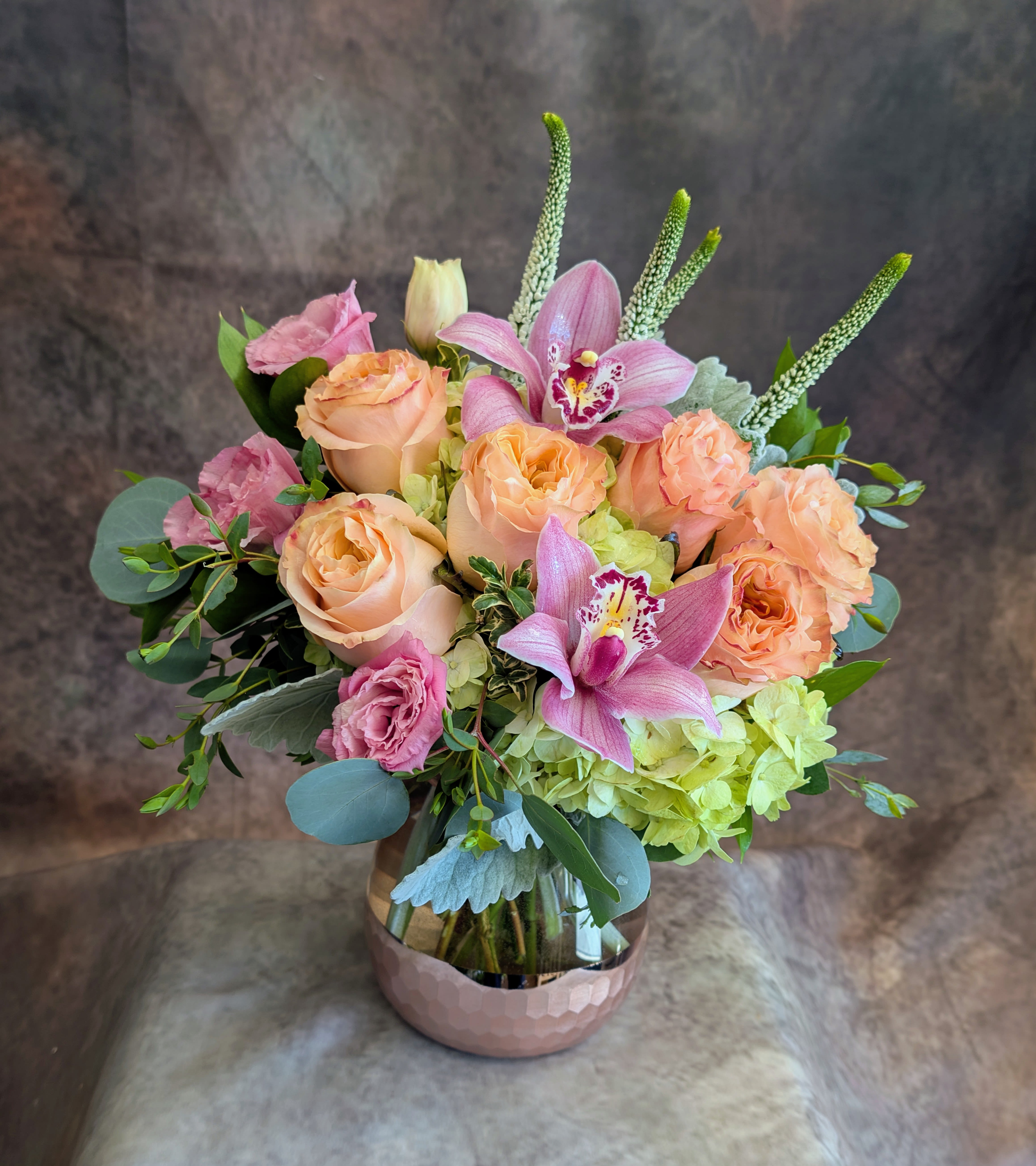 Anya - Softly romantic and effortlessly refined, Anya is a garden-inspired composition designed to feel like a quiet love note in bloom. Lush peach garden roses unfurl alongside delicate blush lisianthus and a cloud of fresh green hydrangea, while striking pink cymbidium orchids add an elegant, modern focal point. Airy eucalyptus and seasonal greenery create movement and texture, giving the arrangement a natural, just-gathered feel.  Designed in a contemporary glass vessel with a warm rose-gold base, Anya is perfect for celebrating love, anniversaries, birthdays, or simply sending something beautiful “just because.” Each piece is custom-crafted with the freshest blooms available, making every arrangement one-of-a-kind.  Handcrafted in Las Vegas by Windmill Floral Expressions, Anya is available for same-day flower delivery in Las Vegas and Henderson.