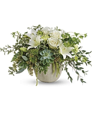 White roses and lilies in a round ceramic vase with trailing greenery