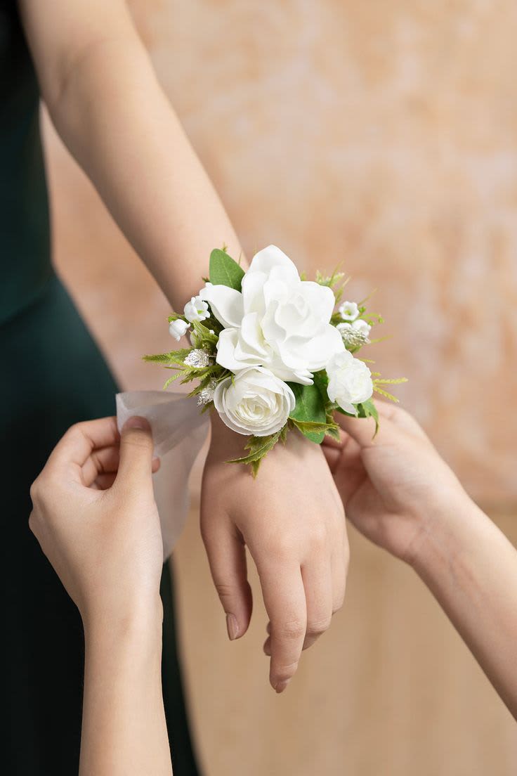 White rose wrist corsage with greenery being tied onto a person's wrist