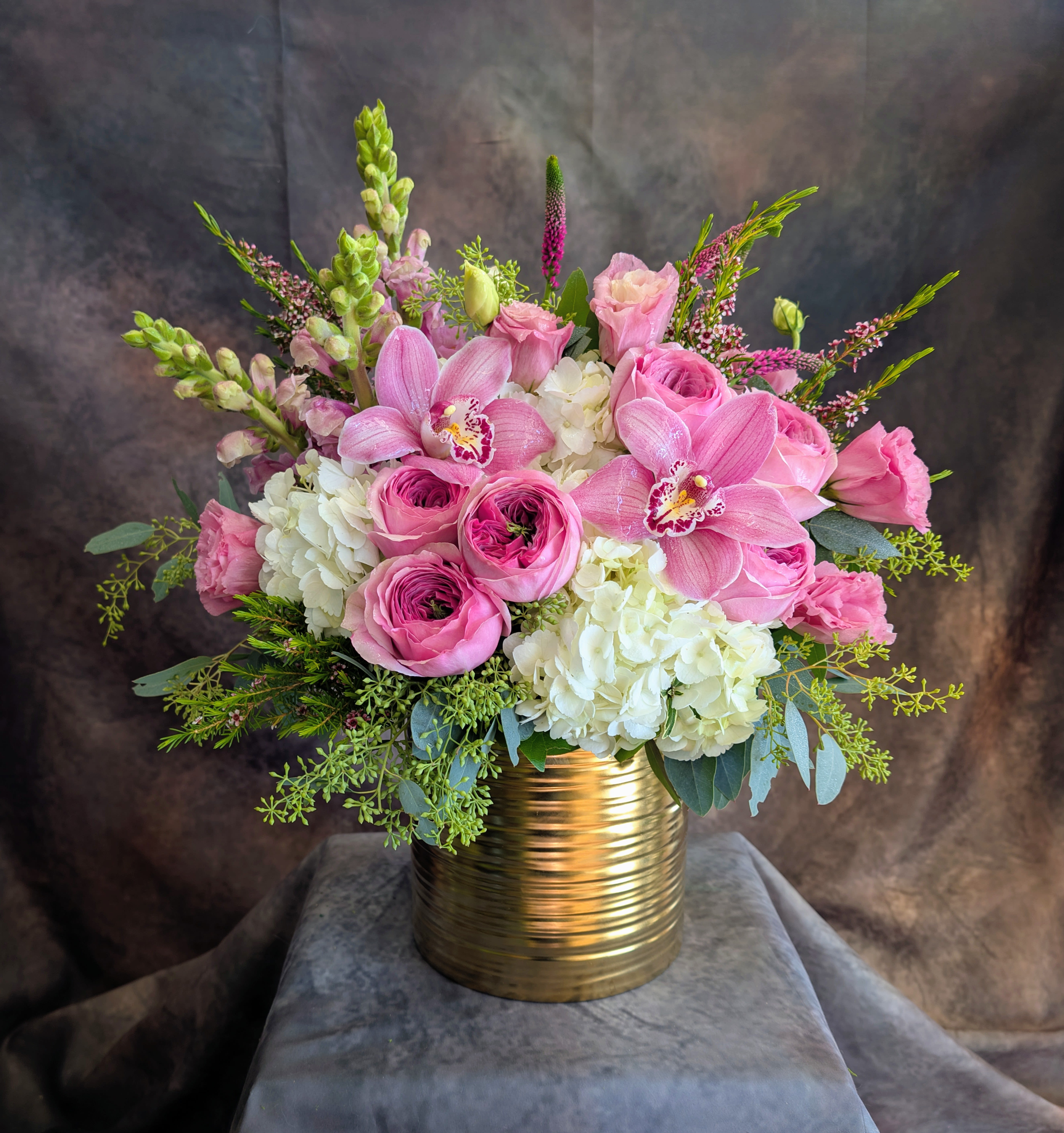 Annika - Soft, romantic, and effortlessly luxurious, Annika is a lush garden-style floral arrangement designed in elegant shades of blush pink and creamy white. Featuring premium Peonikiss roses—known for their full, peony-like blooms—this design is complemented by lisianthus, white hydrangea, and striking pink cymbidium orchids for a refined, modern focal point. Accents of snapdragons, veronica, and fresh eucalyptus add height, texture, and a naturally airy, gathered look.  Arranged in a contemporary gold vessel, Annika is perfect for romantic occasions, anniversaries, birthdays, or sending a soft, feminine statement “just because.” Its timeless palette and premium blooms make it an ideal choice for anyone seeking luxury flower delivery in Las Vegas.  Handcrafted in Las Vegas by Windmill Floral Expressions, a locally owned florist established in 1991, each arrangement is custom-made with the freshest flowers available—no premade designs, always one-of-a-kind.