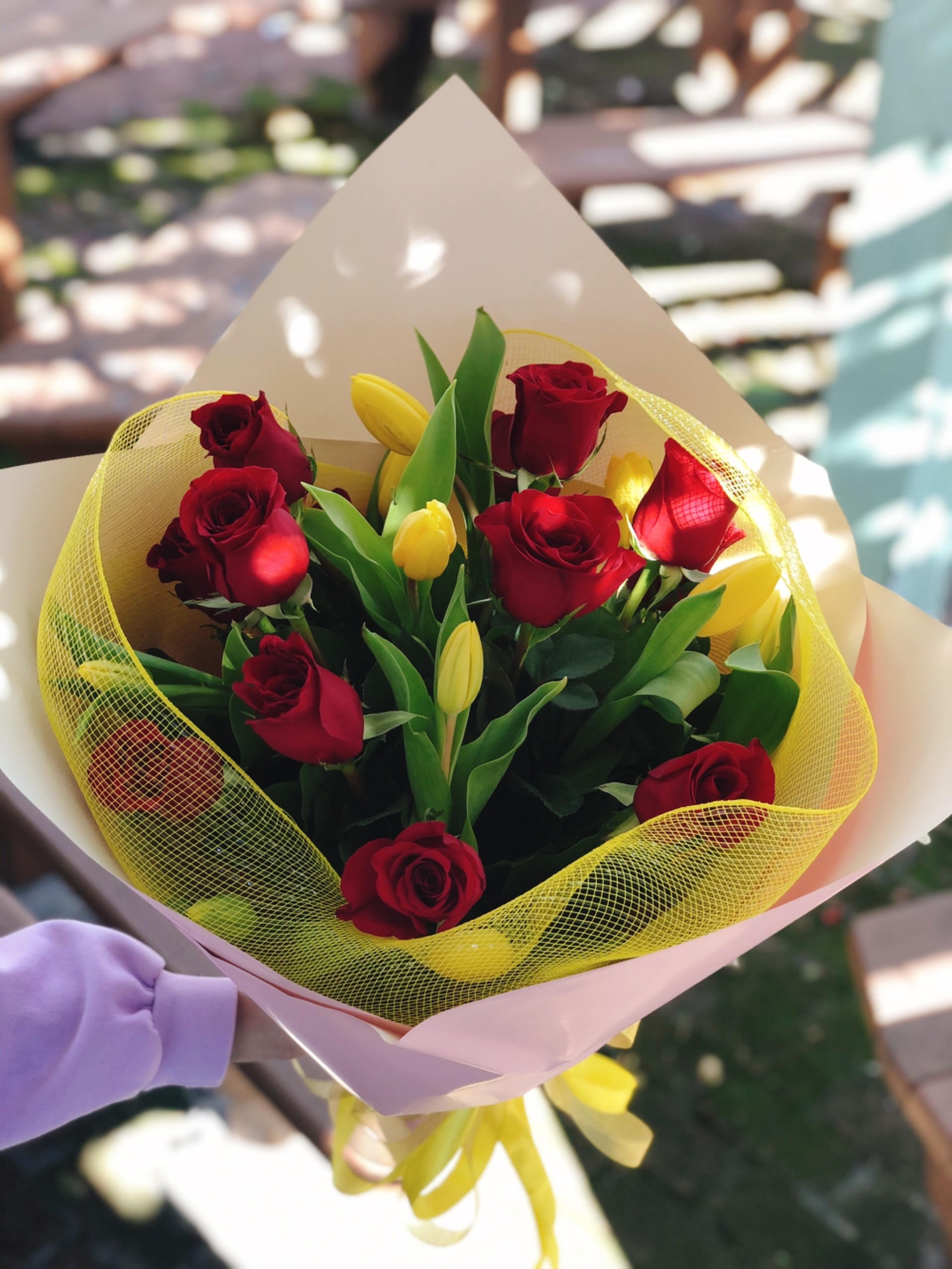 Bouquet of red roses and yellow tulips wrapped in pink paper