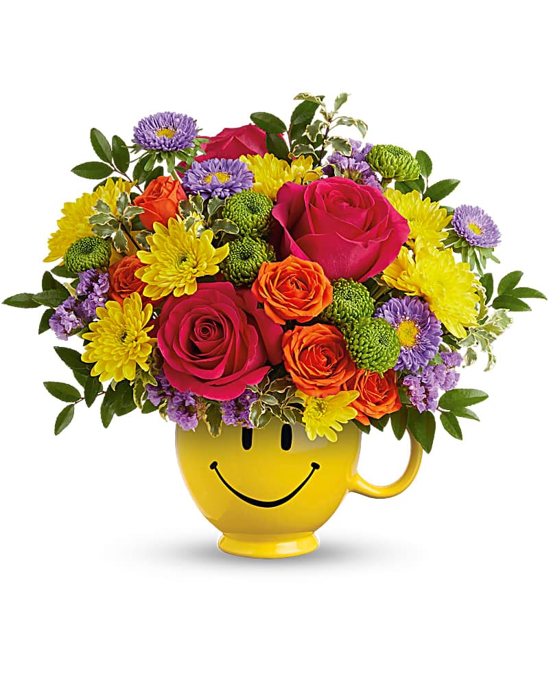 Fiesta Mug - A burst of sunny cheer, this flower arrangement is a playful birthday bouquet or just-because gift that instantly brightens someone's day. The Fiesta Smiley Face arrangement pairs hot pink and orange roses with sunny yellow chrysanthemums and purple aster-like blooms, gathered in a bright yellow ceramic mug printed with a black smiley face-perfect for birthdays, congratulations, or to say "thinking of you" with a big grin.  