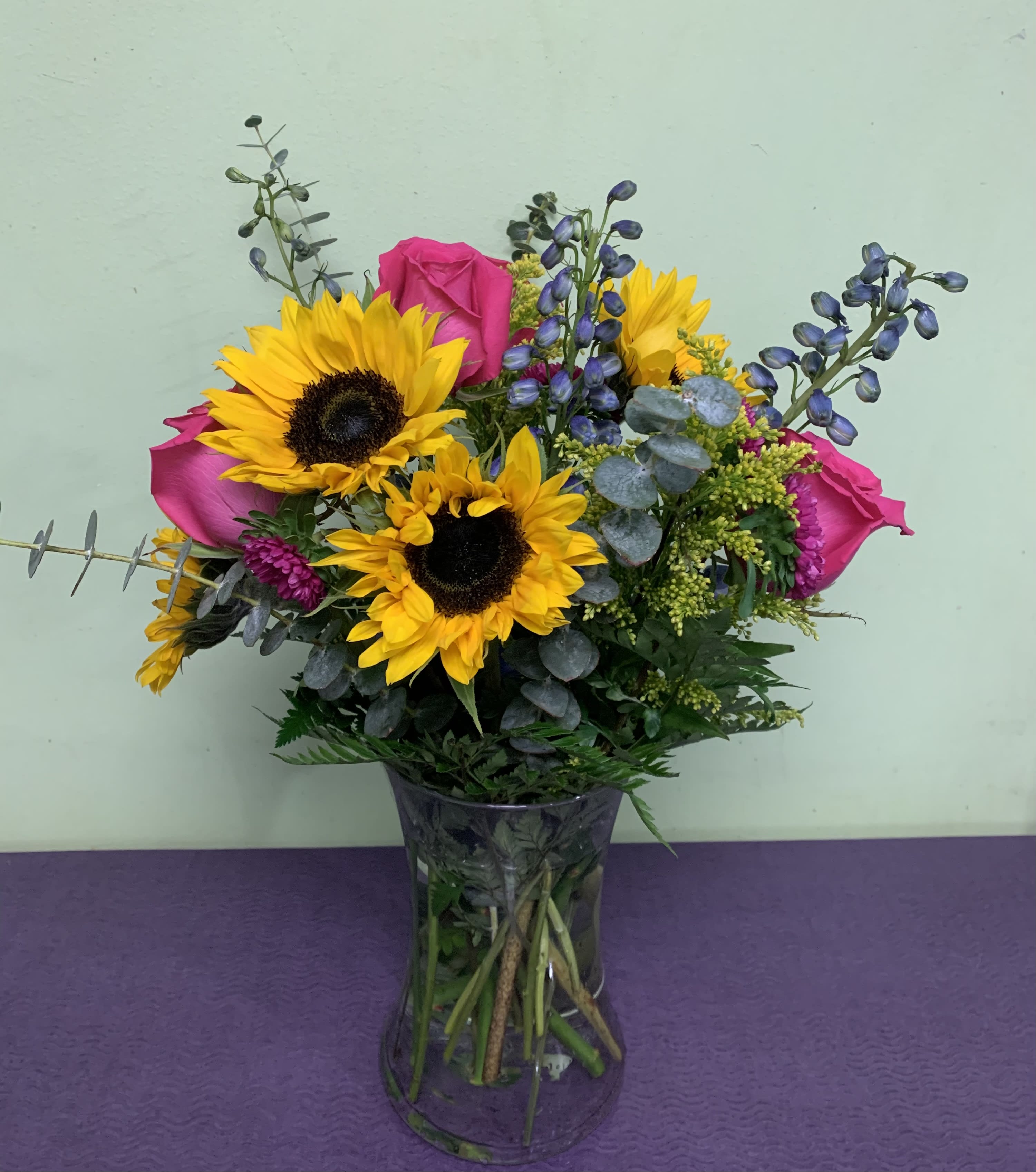 Bouquet of sunflowers, pink roses, and purple accents in a glass vase