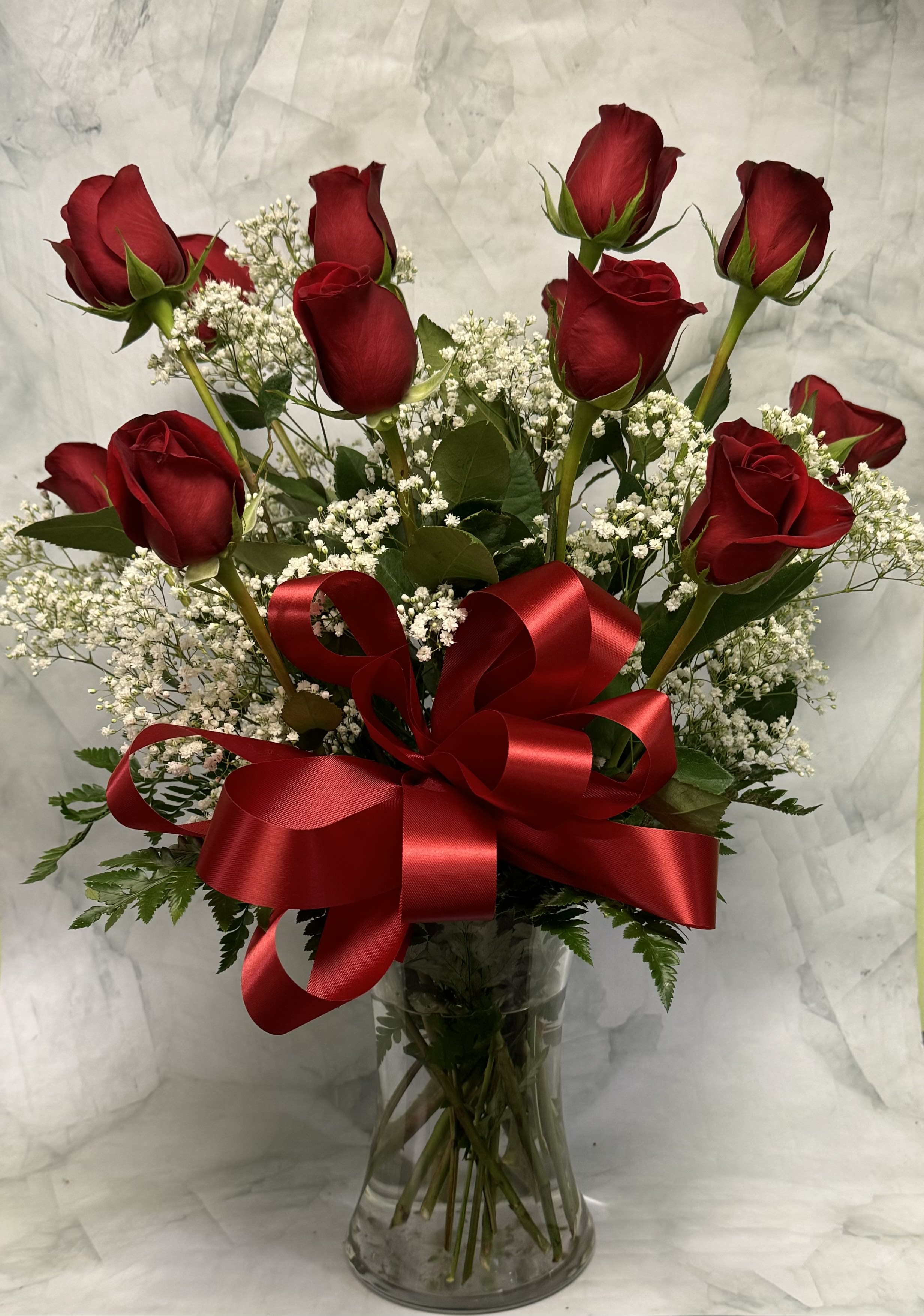 Red roses in a clear glass vase with baby's breath and a red ribbon bow