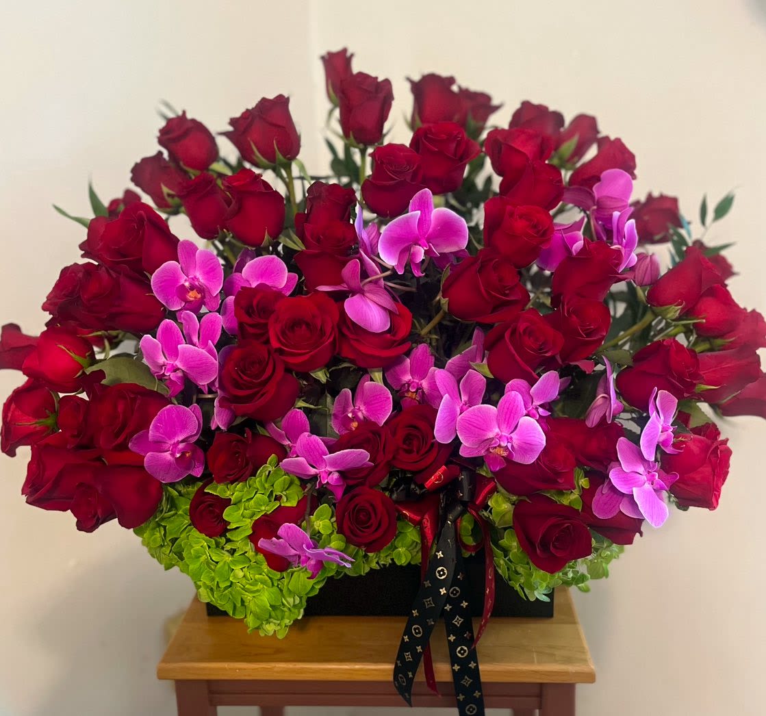 Your Smile Bouquet - A lush cascade of deep red roses and bright pink orchids set against a cushion of vivid green hydrangeas creates an immediate, romantic impact-perfect as a birthday bouquet, anniversary arrangement, or a heartfelt "I'm sorry" gift. Presented for Mother's Day or Valentine's Day, this flower arrangement reads as both dramatic and intimate; the person you're thinking of will feel seen and celebrated the moment it arrives.  Flowers are densely arranged in a low, wide black rectangular box tied with a decorative ribbon, giving the composition a polished, gift-ready look that sits beautifully on a dining table or bedside. The mix of velvety roses, sculptural orchids, and full hydrangea blooms offers bold color contrast and rich texture without being tall or fussy, making it especially suited for get well wishes, expressions of love and romance, or a meaningful Best Friends Day or Quinceañera surprise.  This compact, statement-making design is easy to place and care for-keep in a cool room away from direct sun and refresh the water as needed-so it arrives ready to brighten someone's day, whether you're saying congratulations, apologizing, or simply reminding them they matter.
