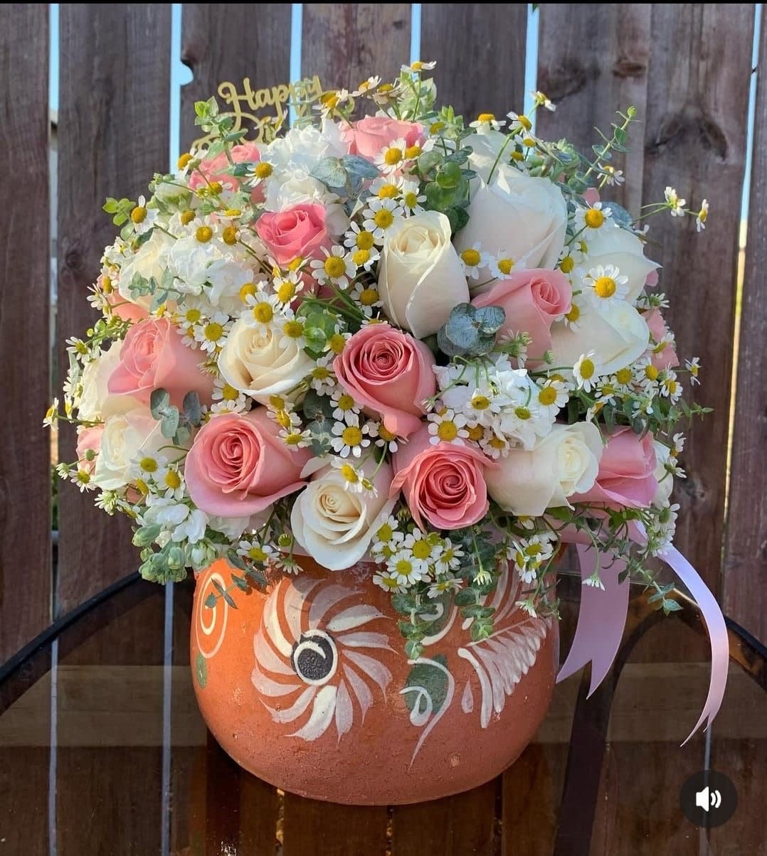 Te amo Madre  - A lush cluster of pink and white roses paired with cheerful white-and-yellow daisies makes this flower arrangement a radiant choice for Mother's Day, a birthday, or any moment you want to say "Te amo, madre." The rounded, abundant composition reads as both romantic and joyful - the sort of gift that will make the person you're thinking of feel cherished and seen.  Soft pastel tones and airy sprigs give the bouquet a light, garden-fresh texture against a painted terracotta pot decorated with floral motifs. A delicate pink ribbon drapes from one side and a decorative pick adds a finishing touch, creating a polished, gift-ready presentation. The mix of roses and daisy-like blooms in pink, white, yellow, and green offers a pleasing contrast of full petals and tiny centers that brightens any room.  Perfect for a loving mother, grandmother, or maternal figure to celebrate a milestone or simply show appreciation, this arrangement arrives arranged and ready to display - no vase hunting required. For best enjoyment, place in a cool spot away from direct sun and refresh the water if you transfer stems; ordering ahead ensures timely delivery for special days like Mother's Day or a birthday.