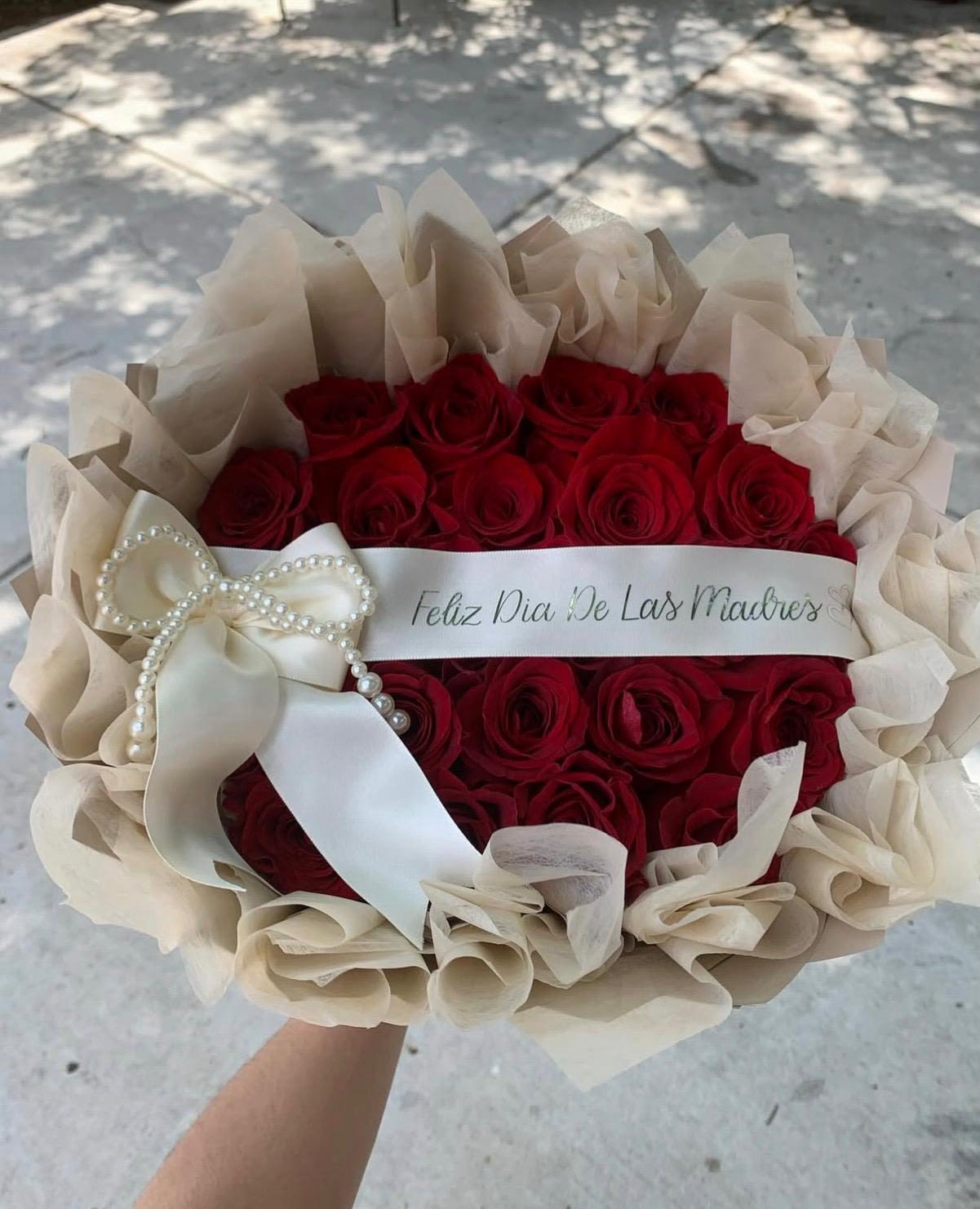 Para mi mama - Deep, velvety red roses gathered in a lush, rounded hand-tied bouquet-perfect as a Mother's Day bouquet or an anniversary roses gift that says "te quiero" with timeless elegance. The intense crimson blooms make a romantic, celebratory statement so the person you're thinking of feels cherished and noticed the moment they see it.  Each bloom is arranged in a dense cluster and wrapped in layered beige tissue that softens the palette and highlights the roses' richness. A wide white satin ribbon finished with a pearl bow gives the presentation a polished, gift-ready look suitable for a formal celebration or a heartfelt surprise. The neutral wrap and classic ribbon let the red roses take center stage while adding refinement and ease for gifting.  Made to be handed straight to Mom, a partner, or someone you adore, this bouquet is the kind of arrangement that marks milestone moments and everyday appreciation alike. Care: keep stems in fresh water, trim ends and replace water every two days to help the roses stay vibrant. Order with confidence for same-day pickup or delivery when available.