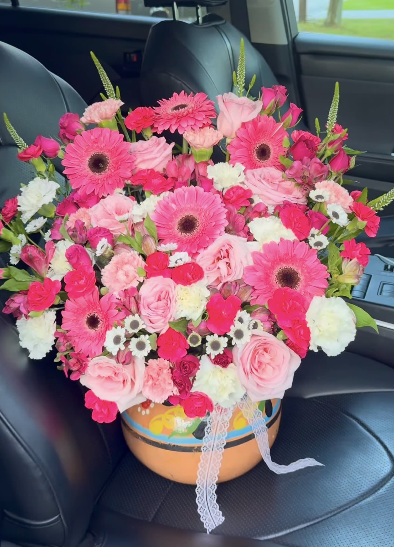 Mi mami es alegre - Bright pink gerbera daisies take center stage in this joyful flower arrangement, making it an ideal birthday bouquet, Mother's Day gift, or anniversary surprise that reads as bright, feminine, and full of affection. The rounded, dense shape brings immediate visual impact so the person you're celebrating will feel noticed and cherished the moment the box is opened.  Soft pink roses, pale carnations, white alstroemeria and daisy accents create a layered, textured mix that balances bold color with tender softness. The flowers are arranged compactly for a full, lush silhouette and presented in a painted round container finished with a delicate lace ribbon for a handcrafted, gift-ready look. The combination of mixed pinks, whites, and blush tones works beautifully for recipients who love classic but playful florals.  Perfect for a mom, sister, close friend, or partner who appreciates cheerful, feminine arrangements, this piece sends a clear message of warmth and celebration. Size and stem lengths are arranged to form a low, rounded centerpiece that's easy to display on a table or counter; care is simple-keep in fresh water and out of direct heat to help blooms last.