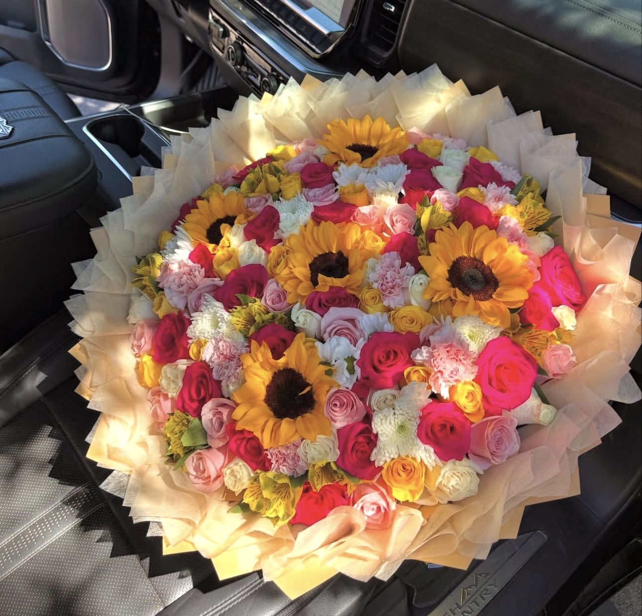Mi rayito de sol  - Sunny sunflowers steal the show in this vibrant birthday bouquet, "Mi rayito de sol," made to brighten a celebration or say congratulations. The round, tightly packed arrangement pairs bold yellow sunflower faces with soft pink, peach, white roses, carnations, and chrysanthemums so the person you're thinking of will feel instantly cheered and noticed.  This full, layered composition is wrapped in pale cream bouquet paper with a wide ruffled edge for a lush, gift-ready presentation. Expect a generous, large arrangement where warm sunflower centers create striking focal points against pastel blooms, giving rich texture and a joyful color contrast that reads beautifully from across the room.  Perfect for birthdays, milestone moments, or as a romantic surprise, this bouquet looks like sunshine delivered - lively, affectionate, and unmistakably celebratory. Order for same-day pickup or delivery when available; keep stems in fresh water and trim before arranging to extend bloom life.