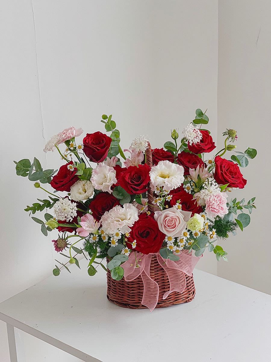 She is spectacular  - A lush, low wicker basket brimming with red and pale pink roses makes this flower arrangement a show-stopping birthday bouquet or anniversary surprise. She is spectacular delivers a romantic, celebratory statement-the kind that makes the person you're thinking of feel noticed and adored-by pairing vivid rose heads with soft white blooms and daisy-like accents for a timeless, feminine look.  This dense, garden-style design layers rounded roses, carnation-like texture, lisianthus and small daisies amid eucalyptus and green filler for depth and movement. The arrangement sits in a woven basket tied with a delicate pink ribbon, creating a compact centerpiece roughly the size of a traditional low basket (suitable for tabletops). Colors are red, pink, white and green, offering a balance of bold and soft tones that reads as both festive and intimate.  Perfect for anniversaries, birthdays, or to say "you're extraordinary," it's the sort of gift that makes her feel truly celebrated the moment it's set in front of her. Because it's arranged low and full, it works well as a centerpiece or as a hand-delivered presentation; keep blooms in fresh water and away from direct heat to extend their life.