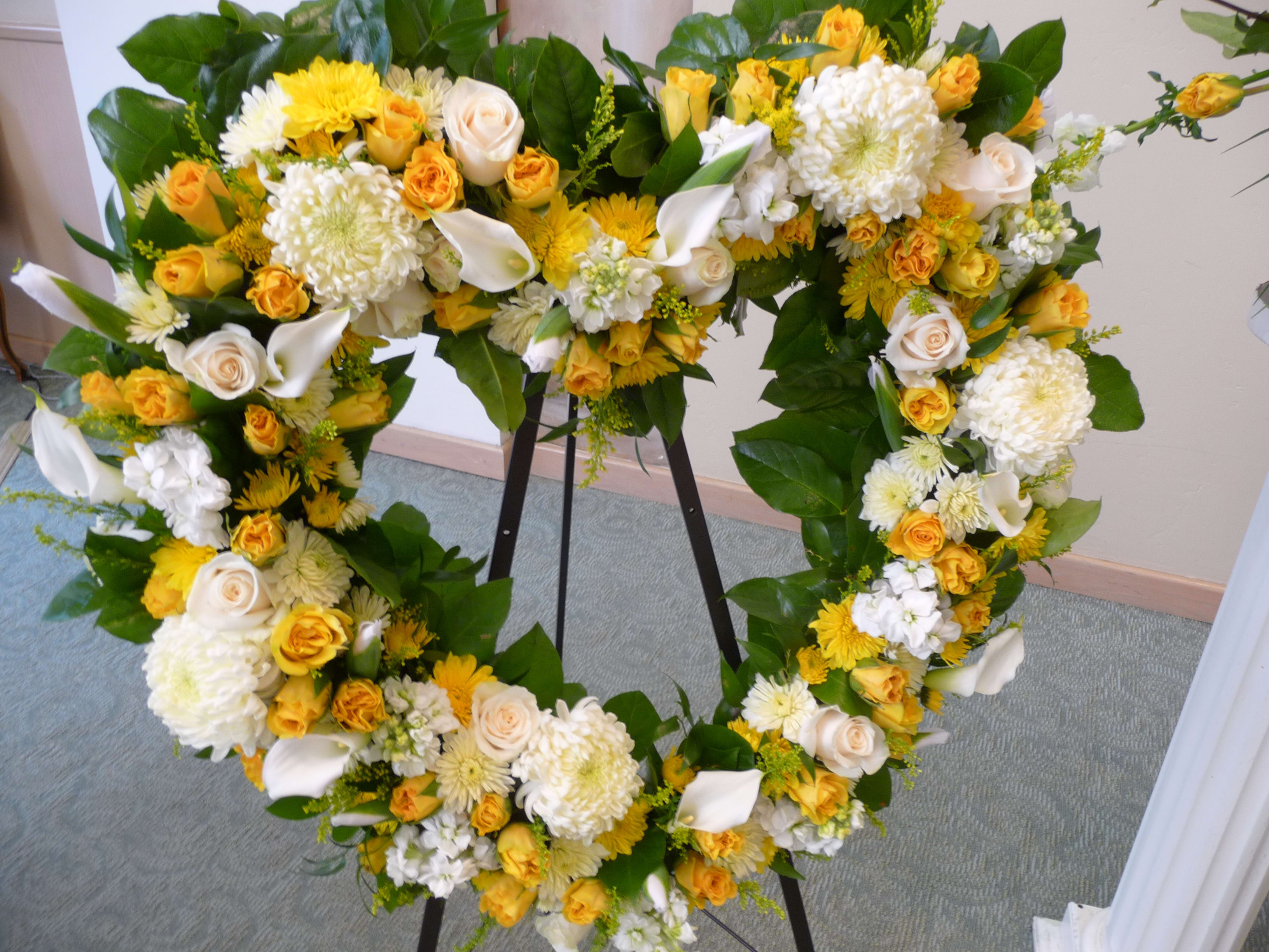 Heart-shaped floral wreath with yellow and white flowers on a stand
