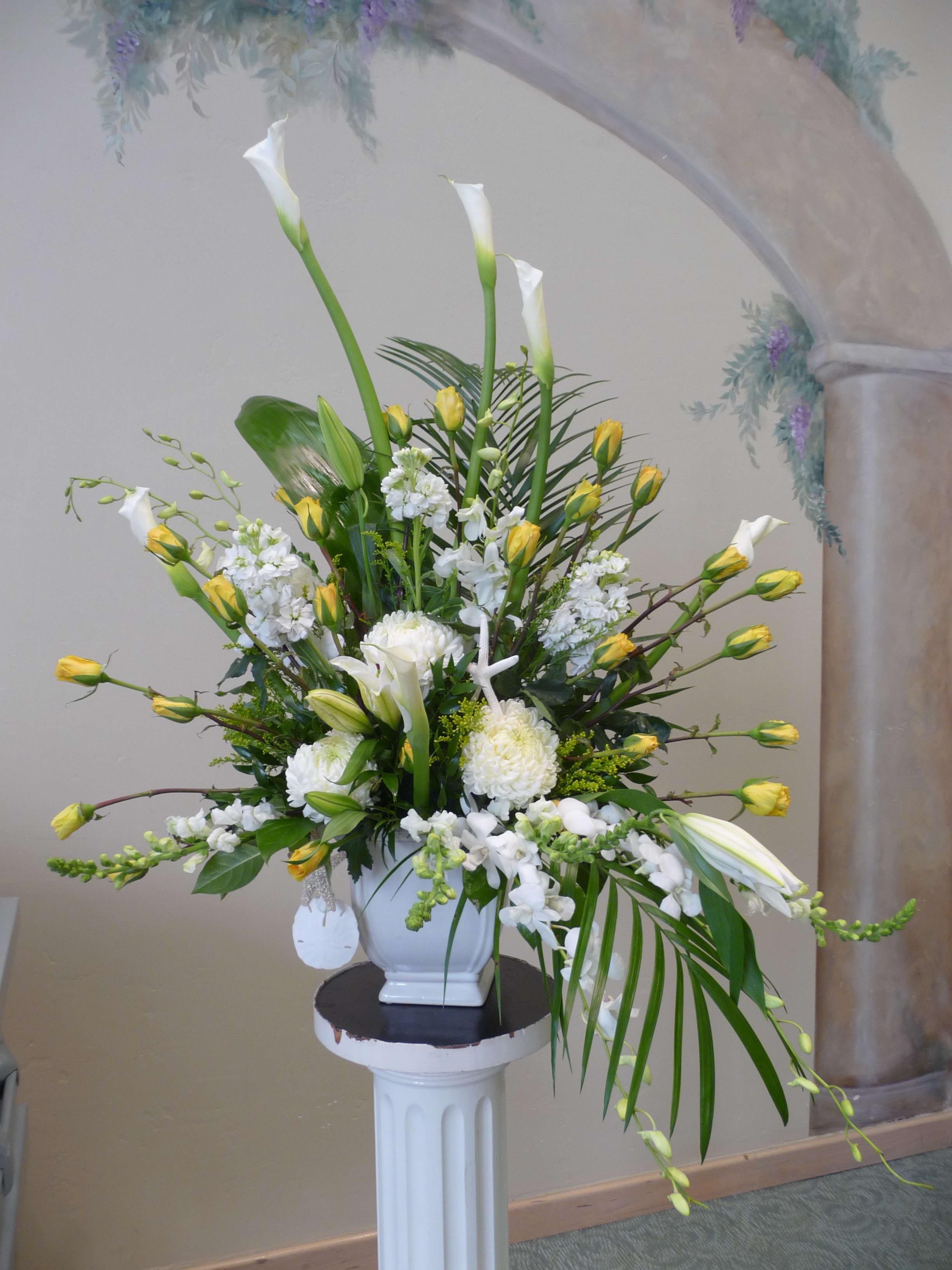 Tall white floral arrangement with yellow accents in a white vase