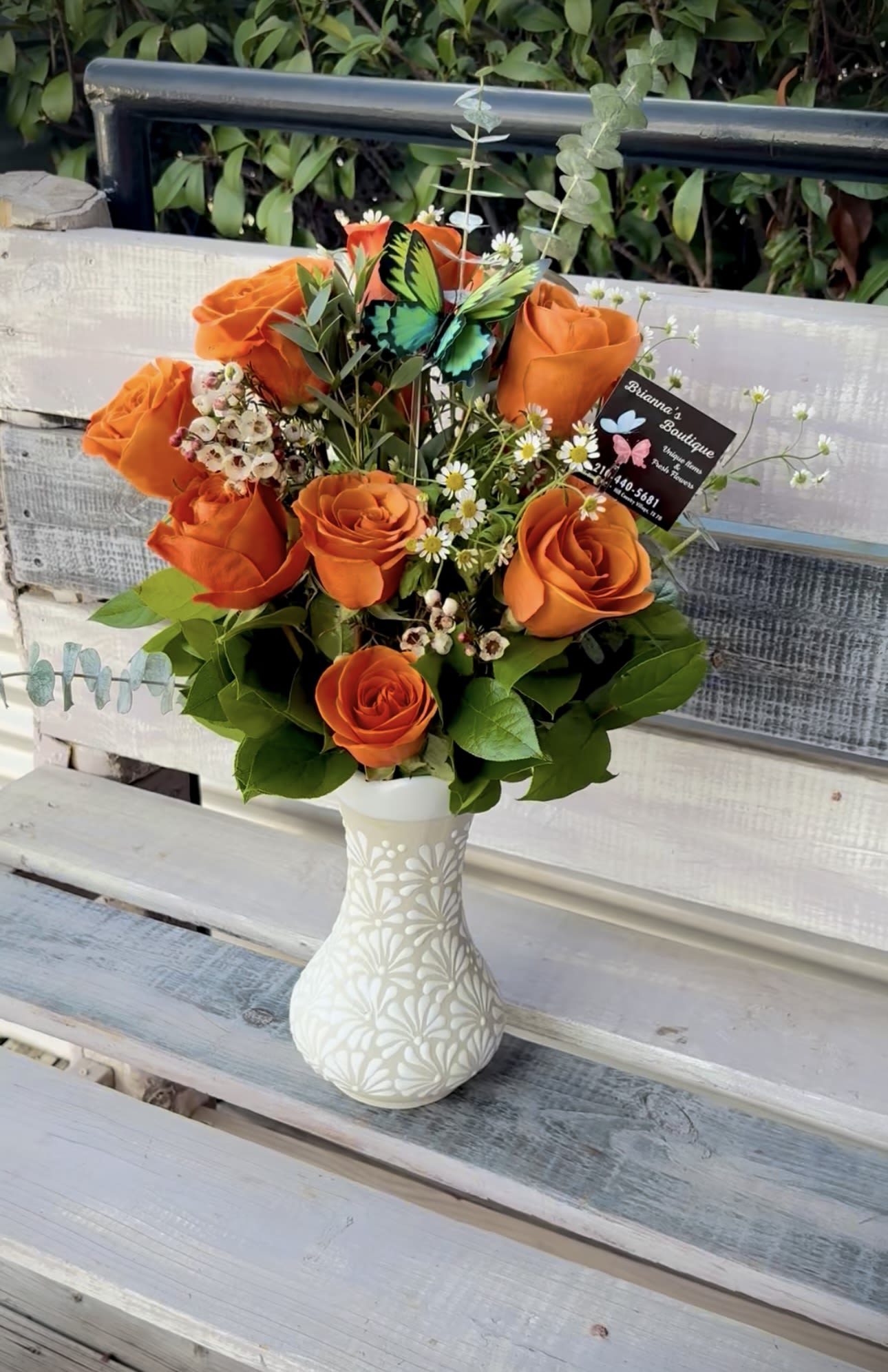 Orange roses arranged in a white vase with small white filler flowers.
