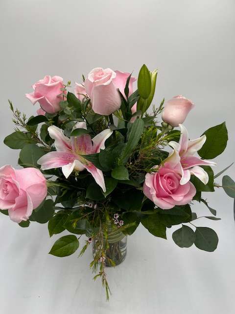 Pink roses and pink lilies arranged in a clear glass vase