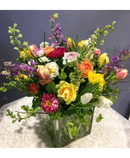 Deluxe Spring Flower Arrangement - This beautiful arrangement is made with a variety of decadent spring flowers: ranunculus, freesia, tulips (we will use Parrot tulips if available), daffodils, larkspur and others. Presented in a glass cube vase.  Includes: Spring Flowers And Folliage, Glass Cube Vase.