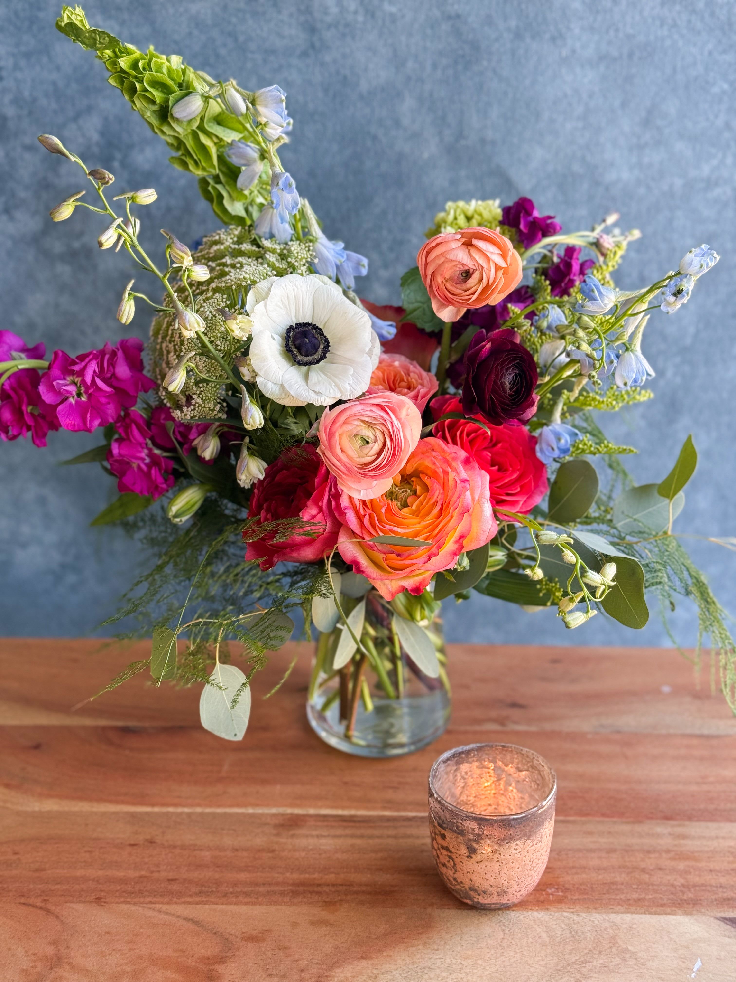 Mixed bouquet in a clear glass vase with pink, orange, white, and blue blooms
