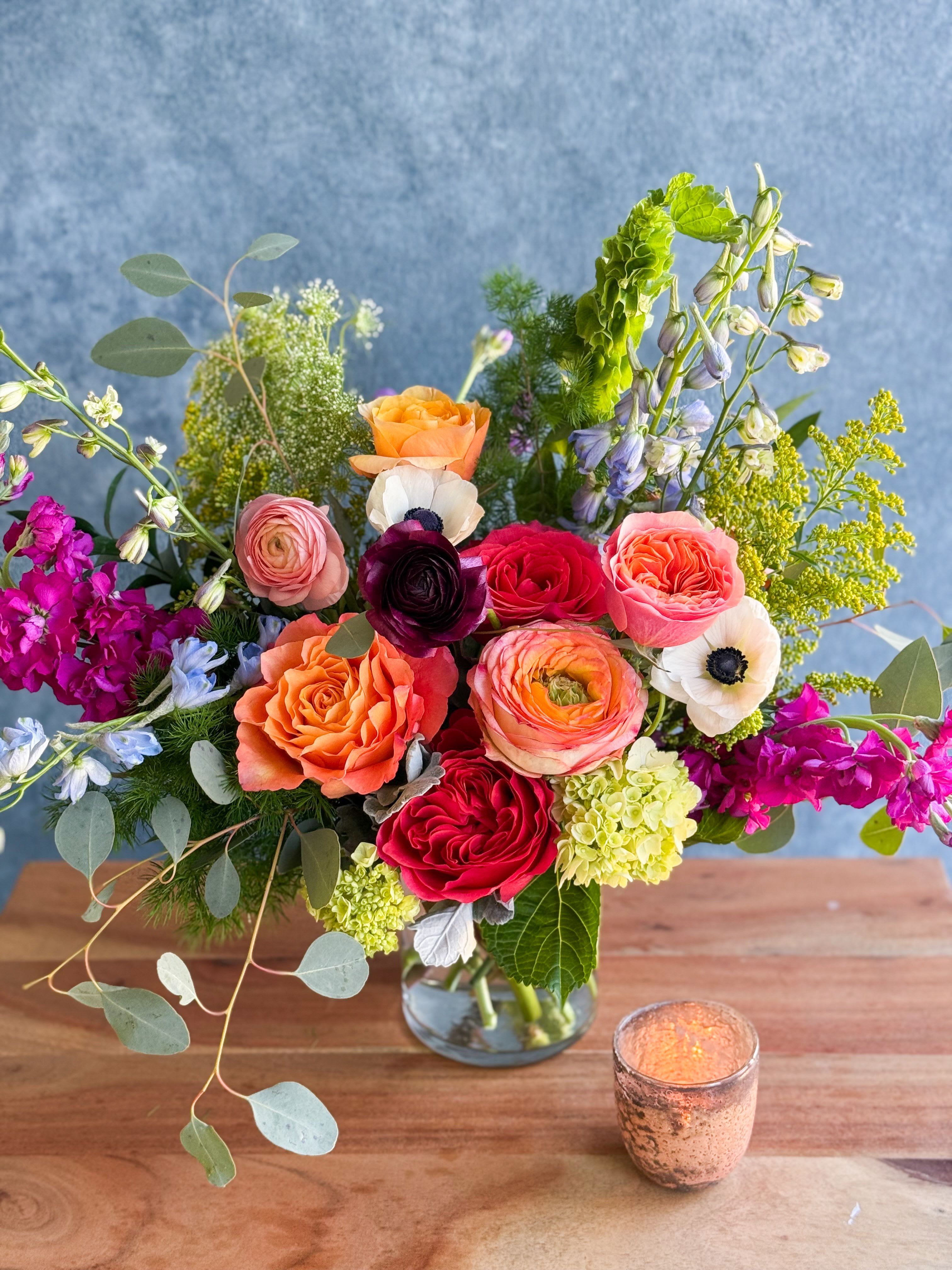 Mixed bouquet of roses and other blooms in a glass vase with a candle nearby