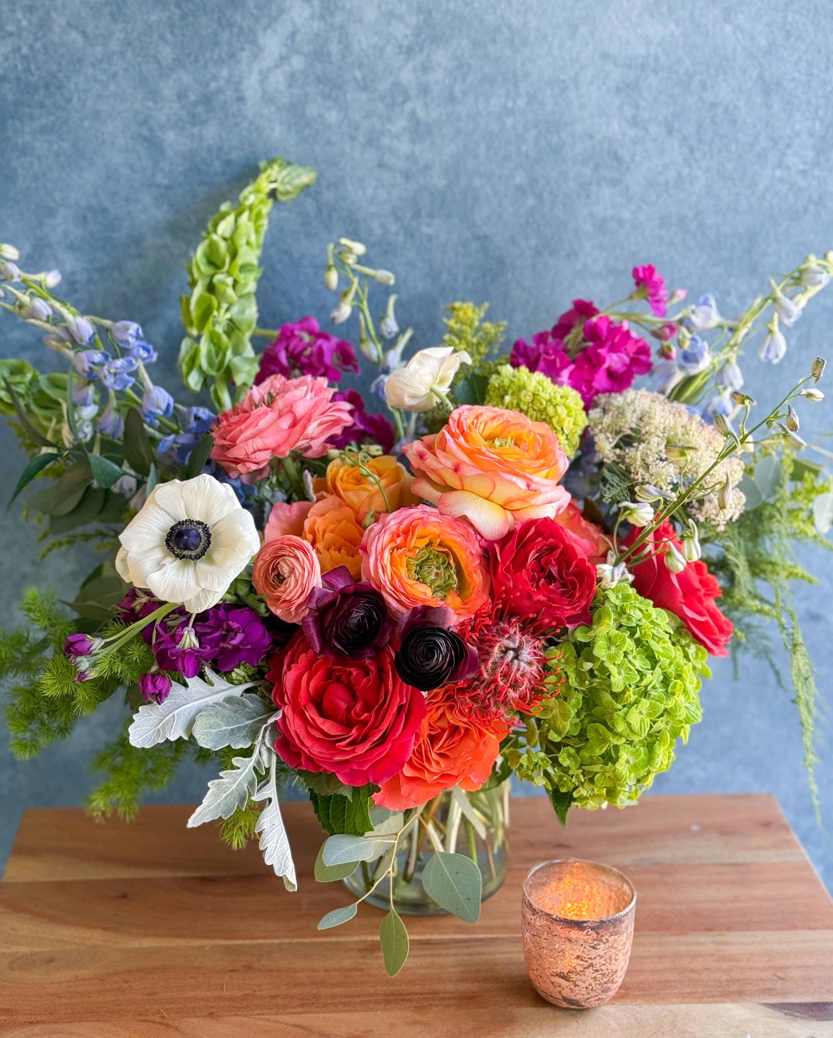Colorful mixed flower arrangement in a glass vase with a candle beside it
