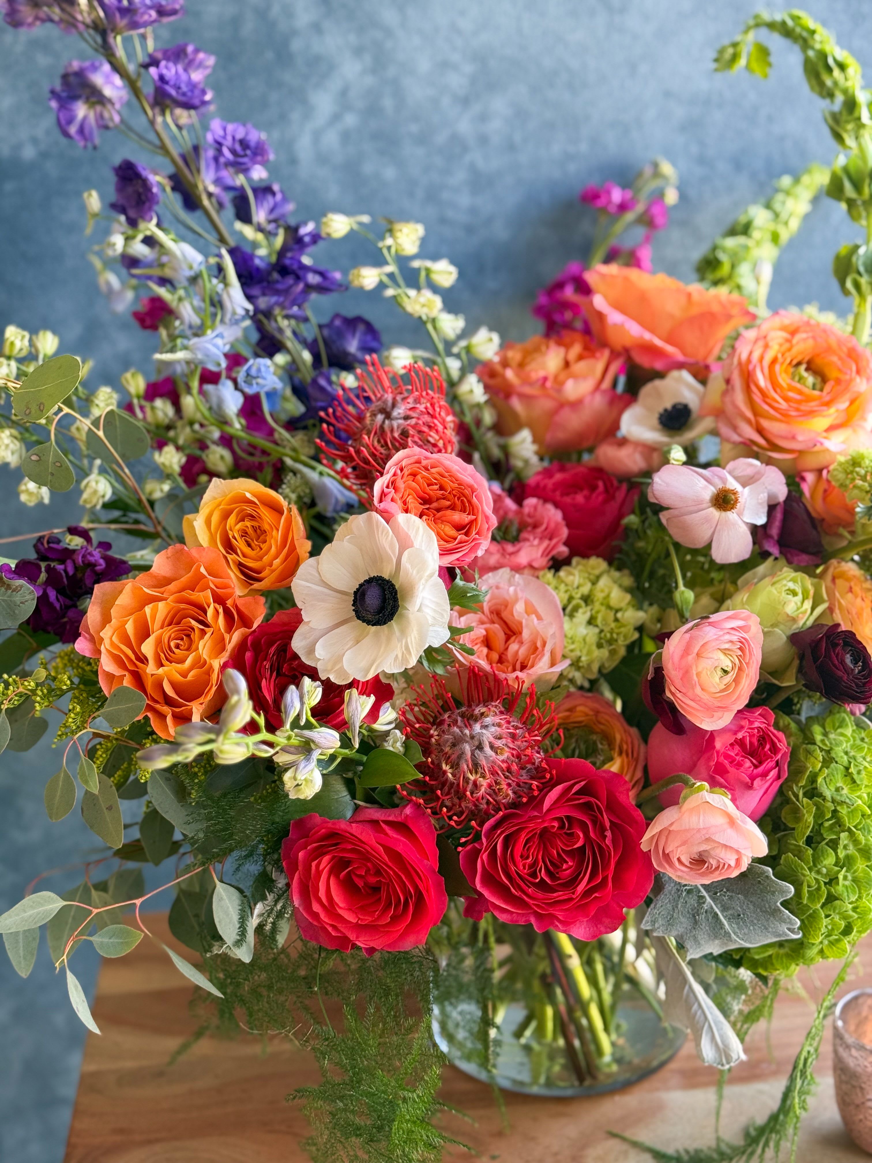 Colorful mixed bouquet of roses, ranunculus, and other blooms in a glass vase