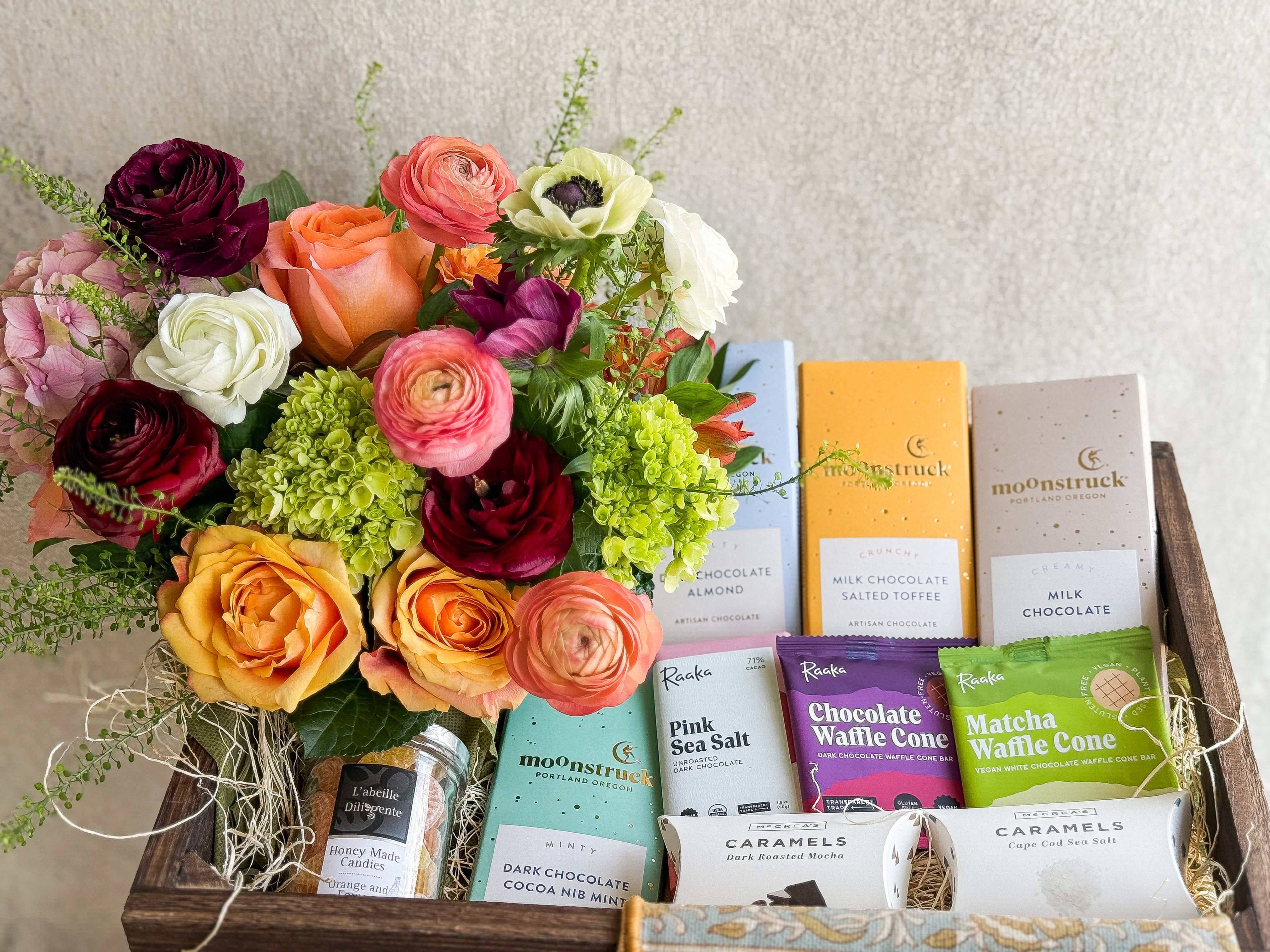 Mixed bouquet beside assorted chocolates and caramels in a wooden gift box