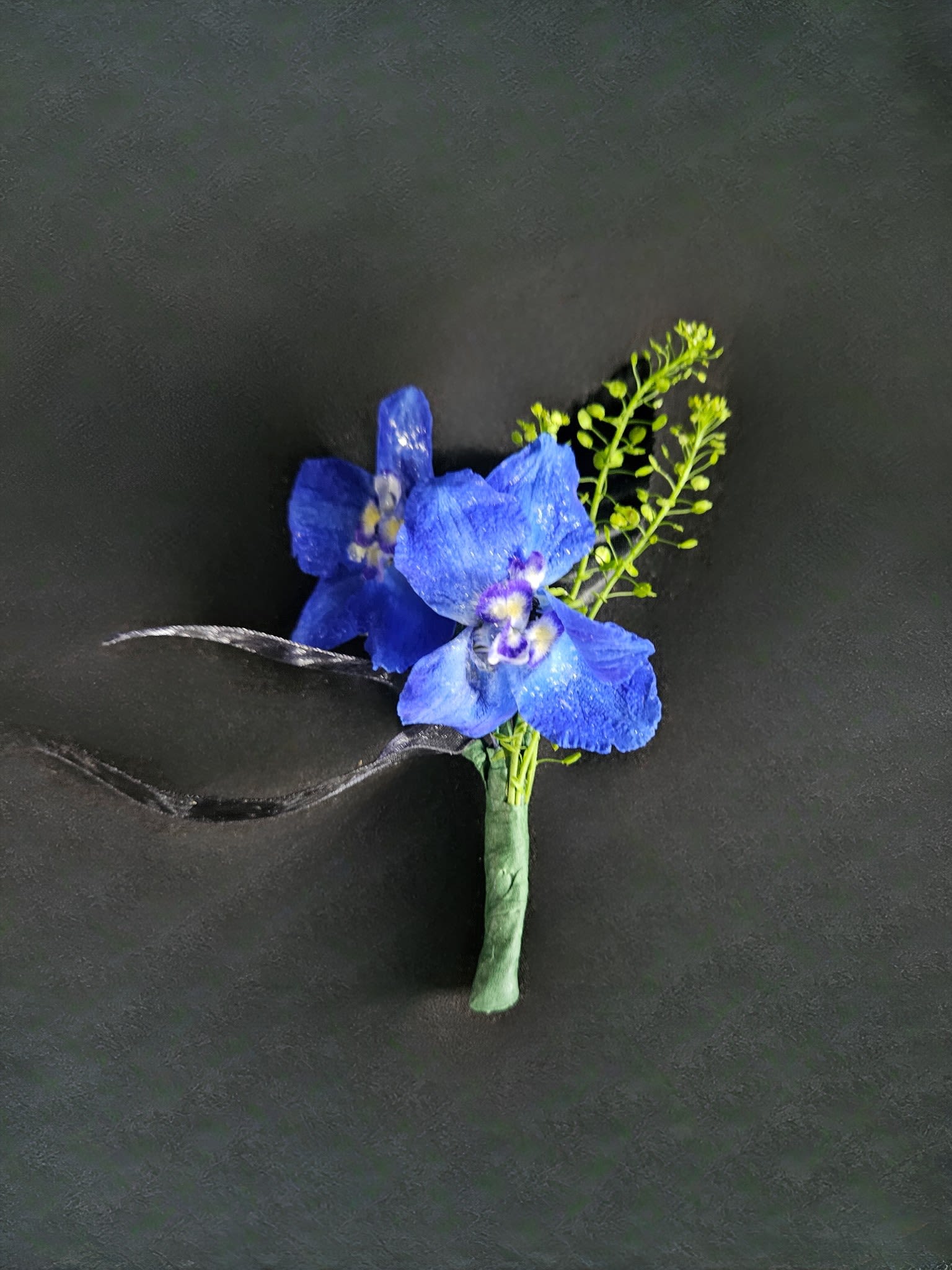 Northmont Dark Blue Delphinium Boutonniere - A naturally blue flower that will compliment any outfit. The only flower color option for this boutonniere is dark blue. Please select up to 2 ribbon colors from the add-on selections you would like included. (Please do not select any of the flower color options)