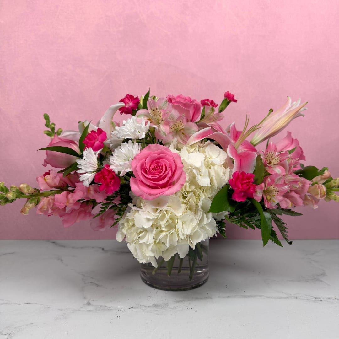 Low pink and white arrangement with roses, lilies, hydrangeas, and other blooms in a clear glass vase