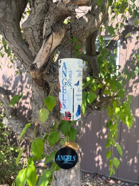 Memorial wind chime with angel-themed text and butterflies hanging from a tree branch